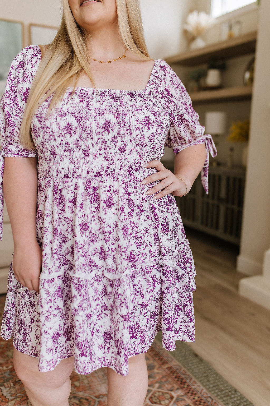 Plus size woman wearing a purple floral dress with puff sleeves and square neckline in cozy home setting