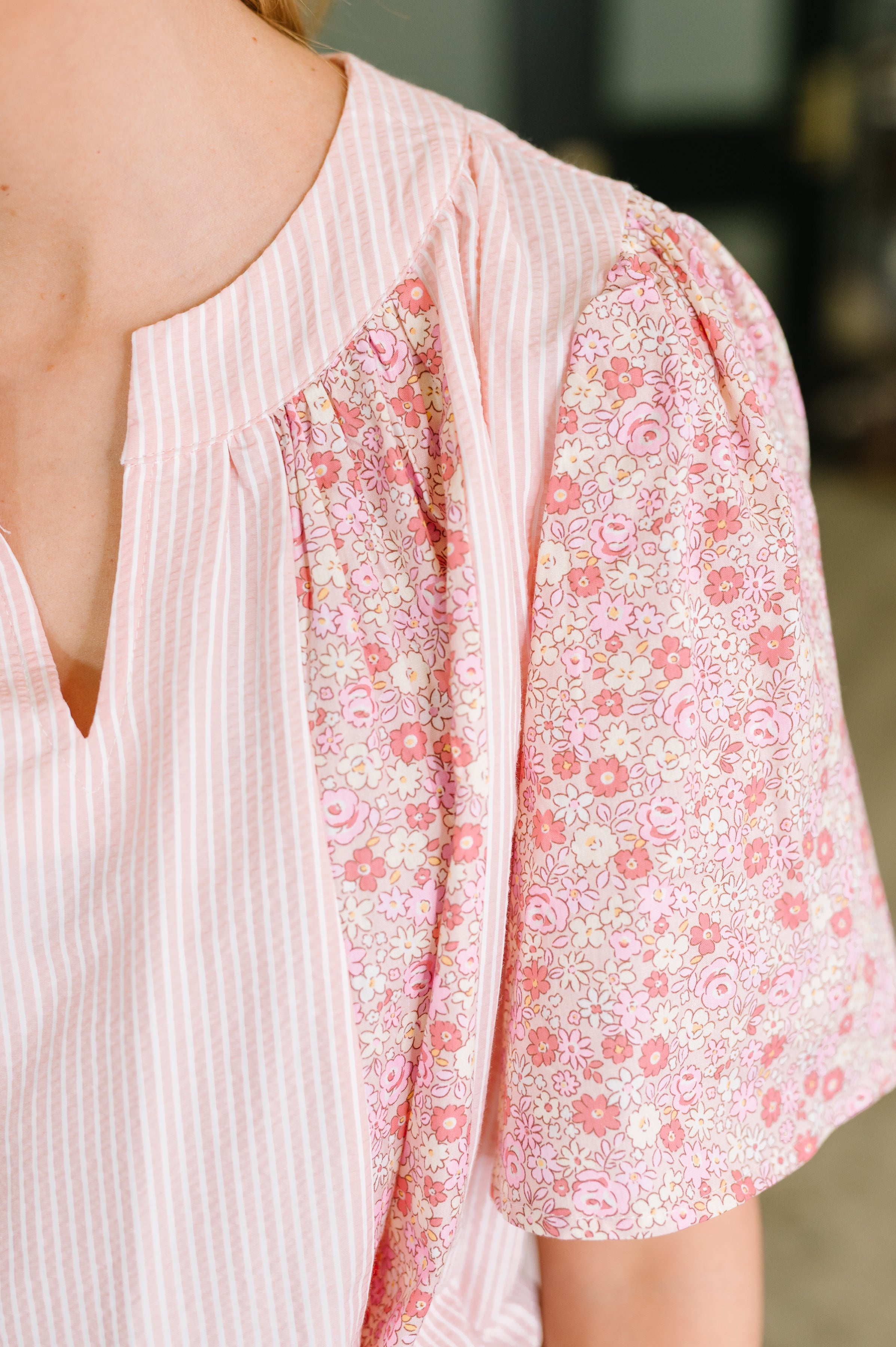Close-up of pink striped blouse with floral puff sleeve and gathered seam detail on shoulder area