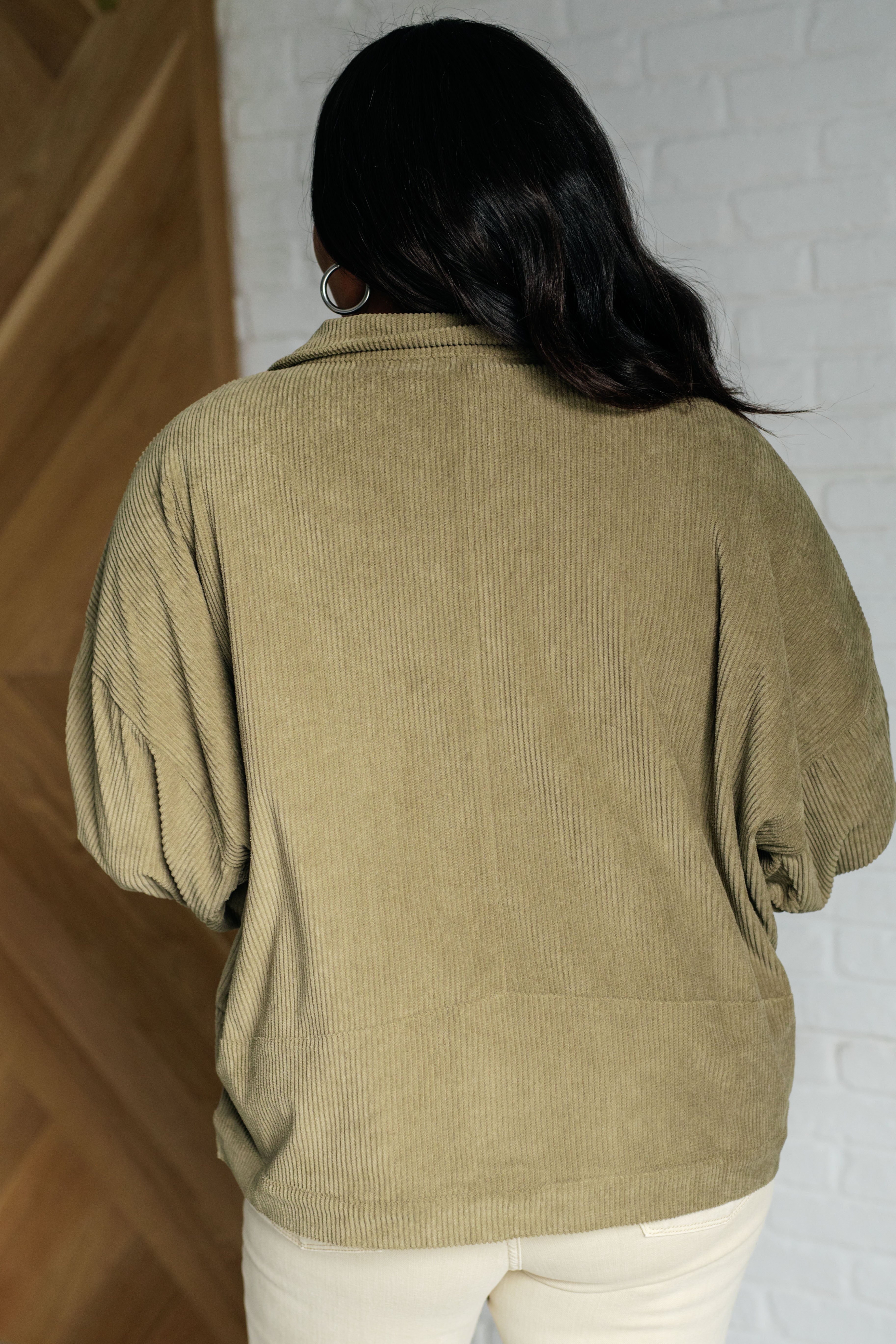 Back view of woman wearing an olive corduroy jacket with balloon sleeves indoors