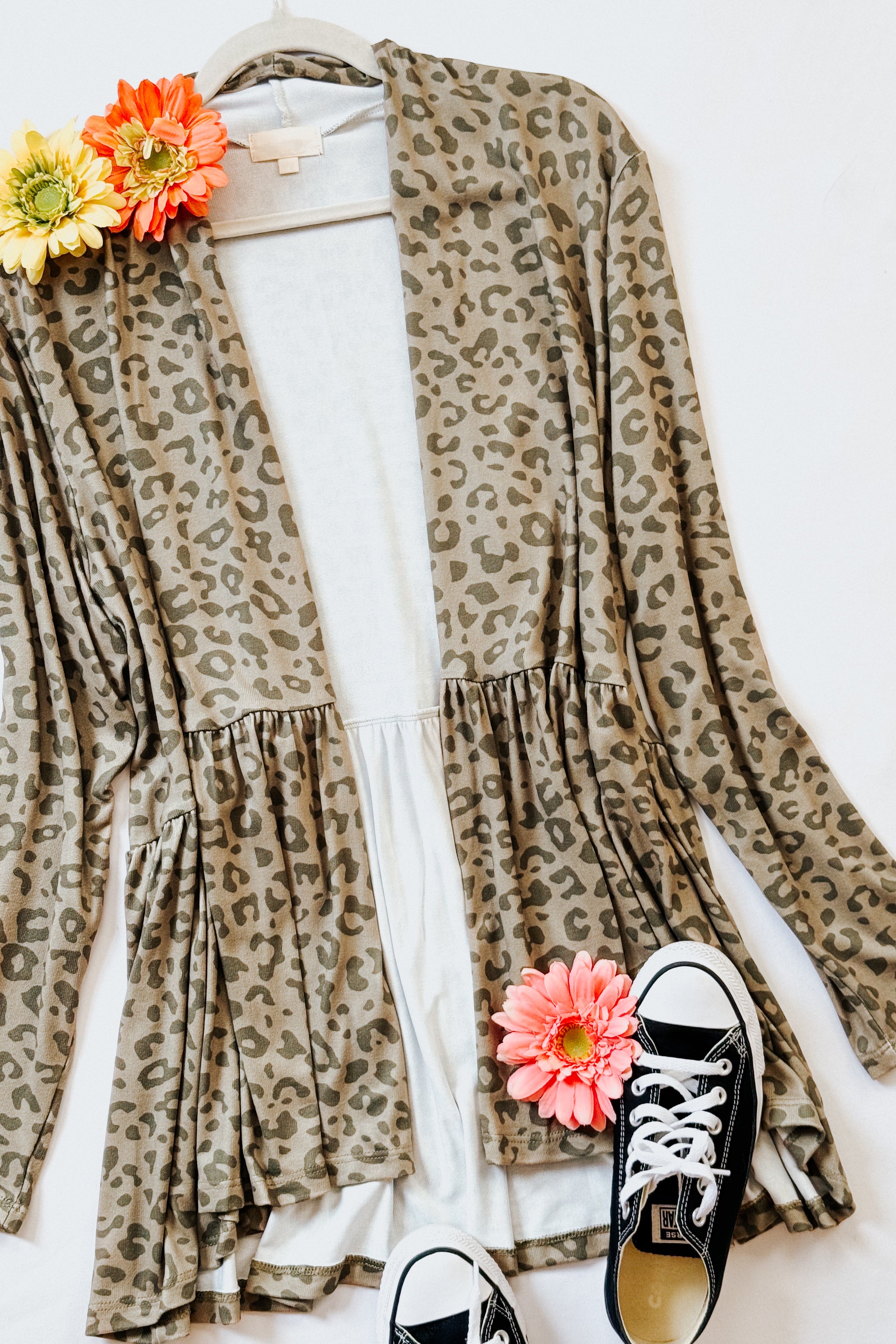 Green leopard print peplum cardigan layered over white top alongside black sneakers and vibrant flowers on white background