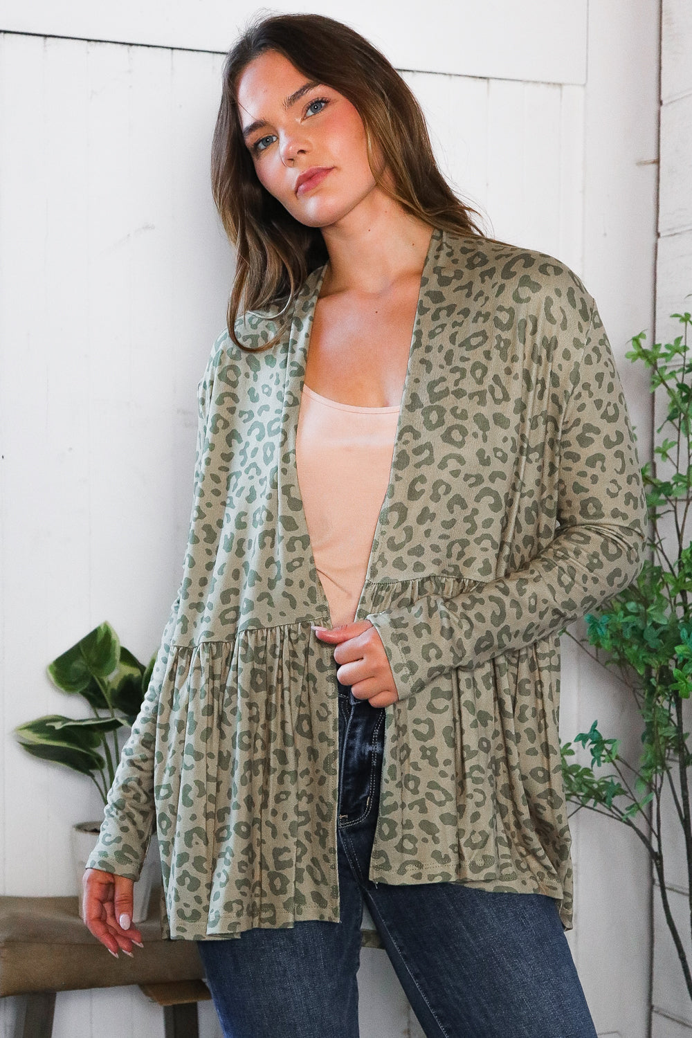 Woman wearing green leopard print peplum cardigan over nude top in relaxed eclectic room with plants and stool nearby