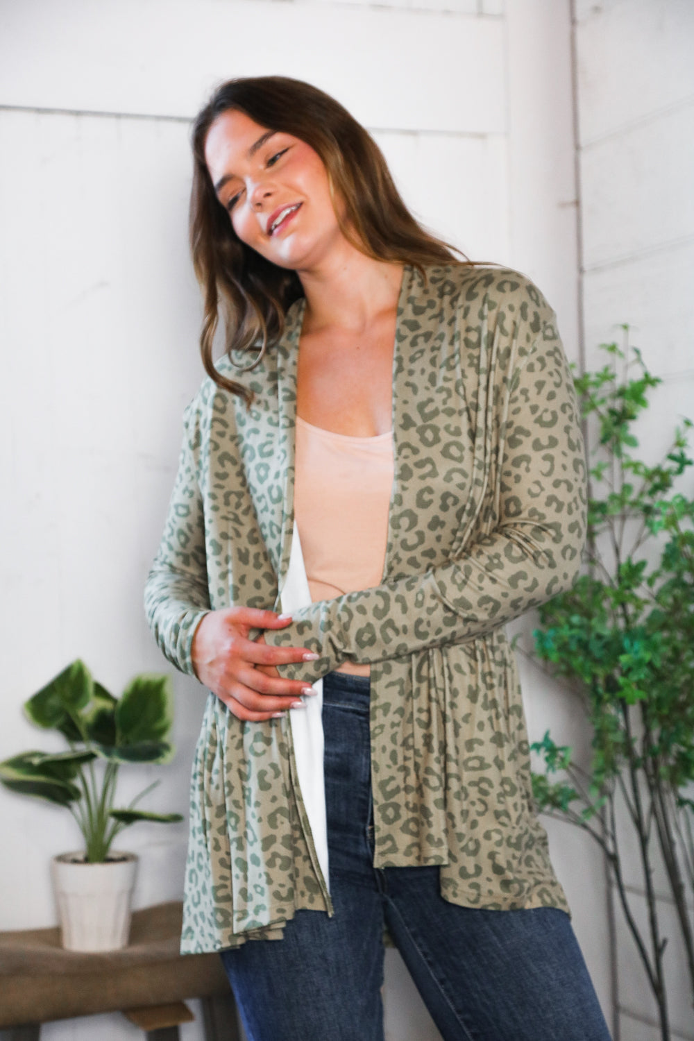 Woman wearing green leopard print peplum cardigan over nude top in relaxed eclectic room with plants nearby