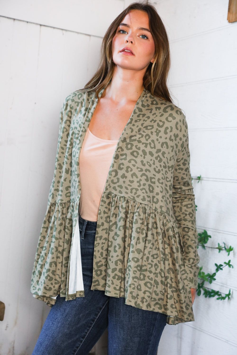 Woman wearing green leopard print peplum cardigan over light beige top in bright eclectic room with greenery nearby
