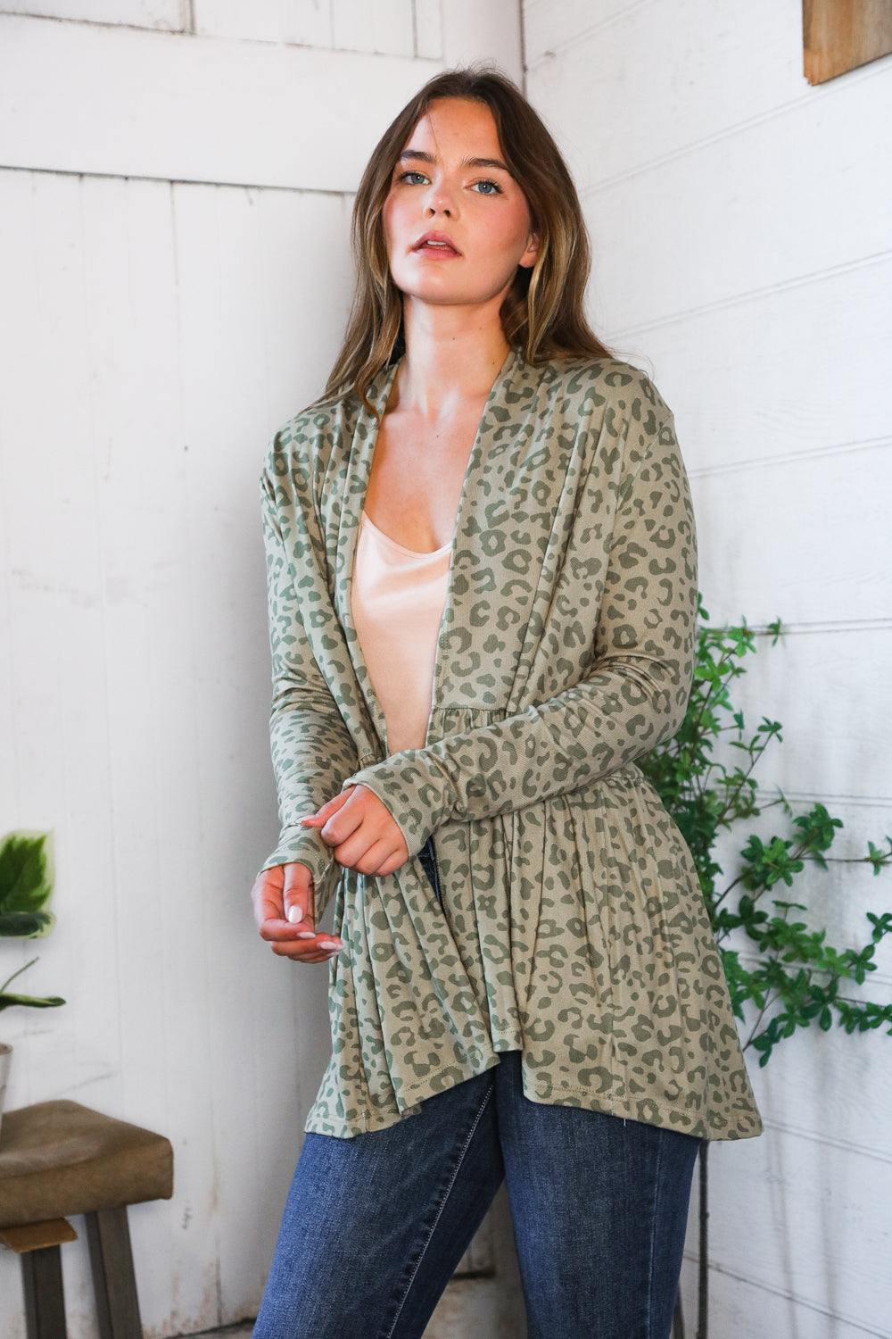 Woman wearing green leopard print peplum cardigan over beige top in light, eclectic room with plants nearby