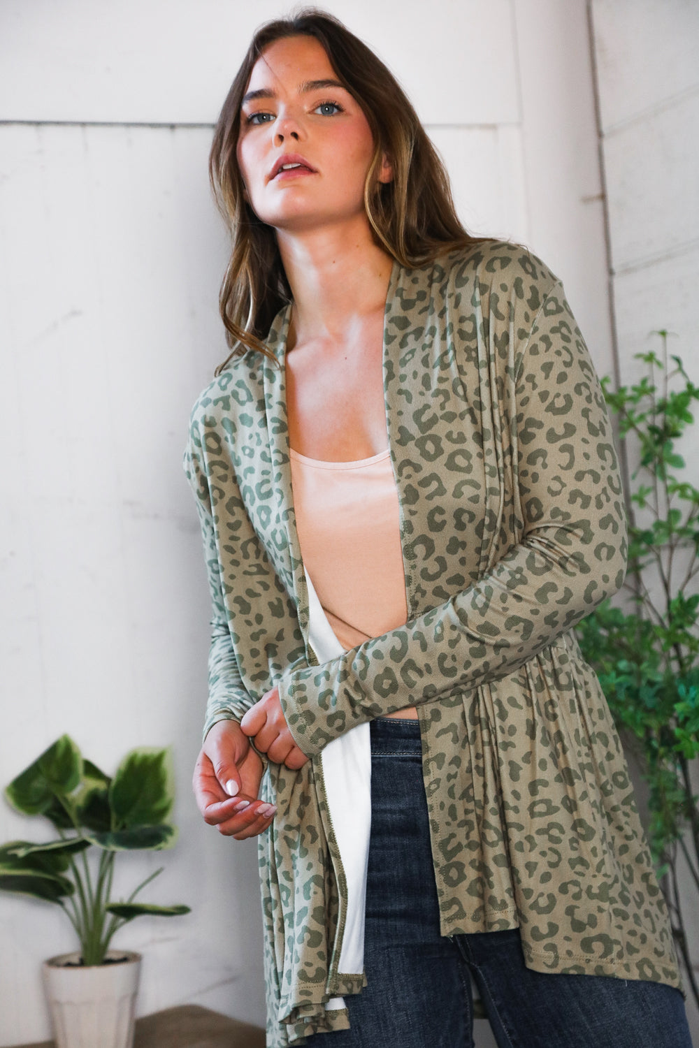 Woman wearing green leopard print peplum cardigan over light beige top in bright, eclectic space with plants nearby