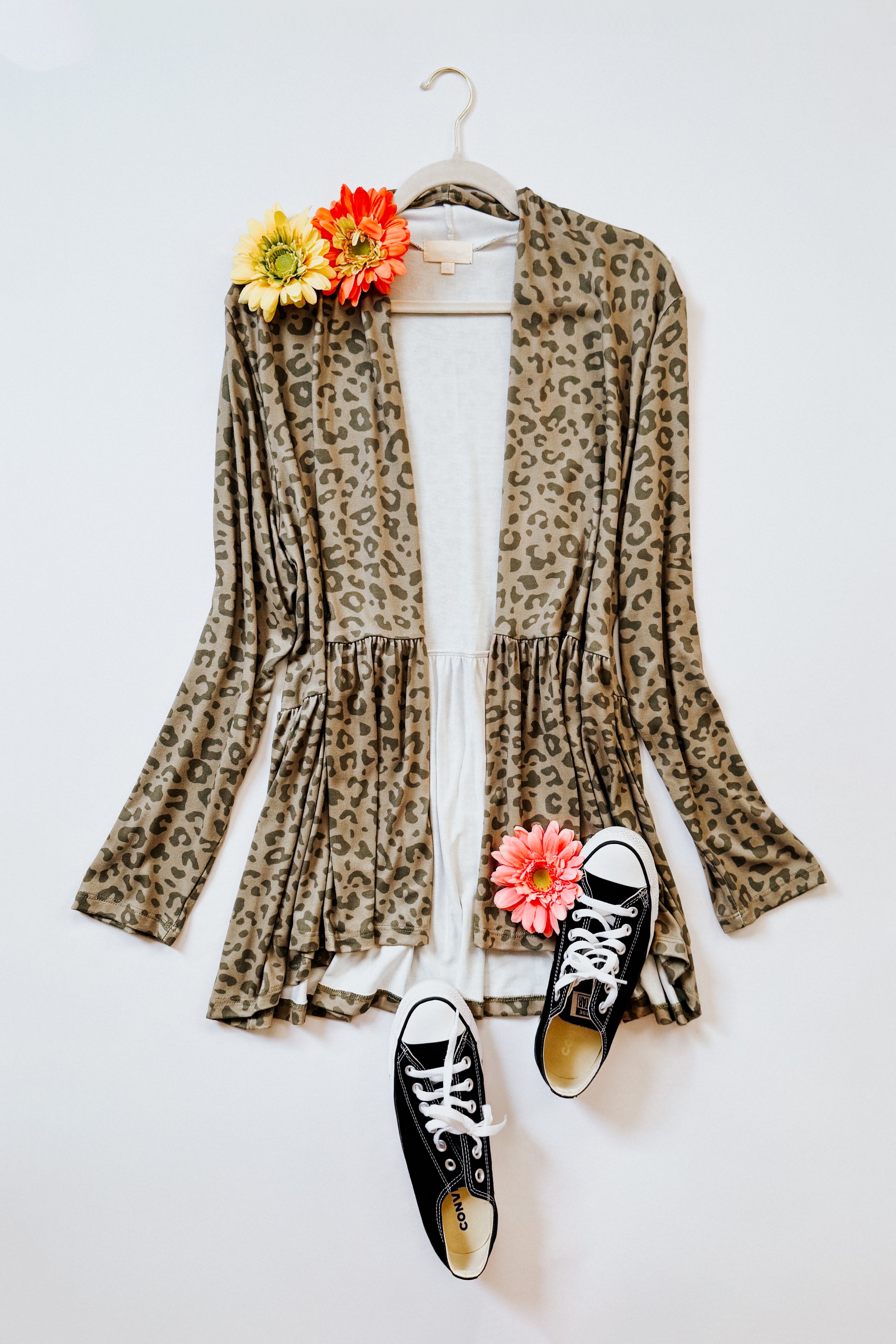 Green leopard print peplum open cardigan styled with black canvas sneakers and bright flowers on white background