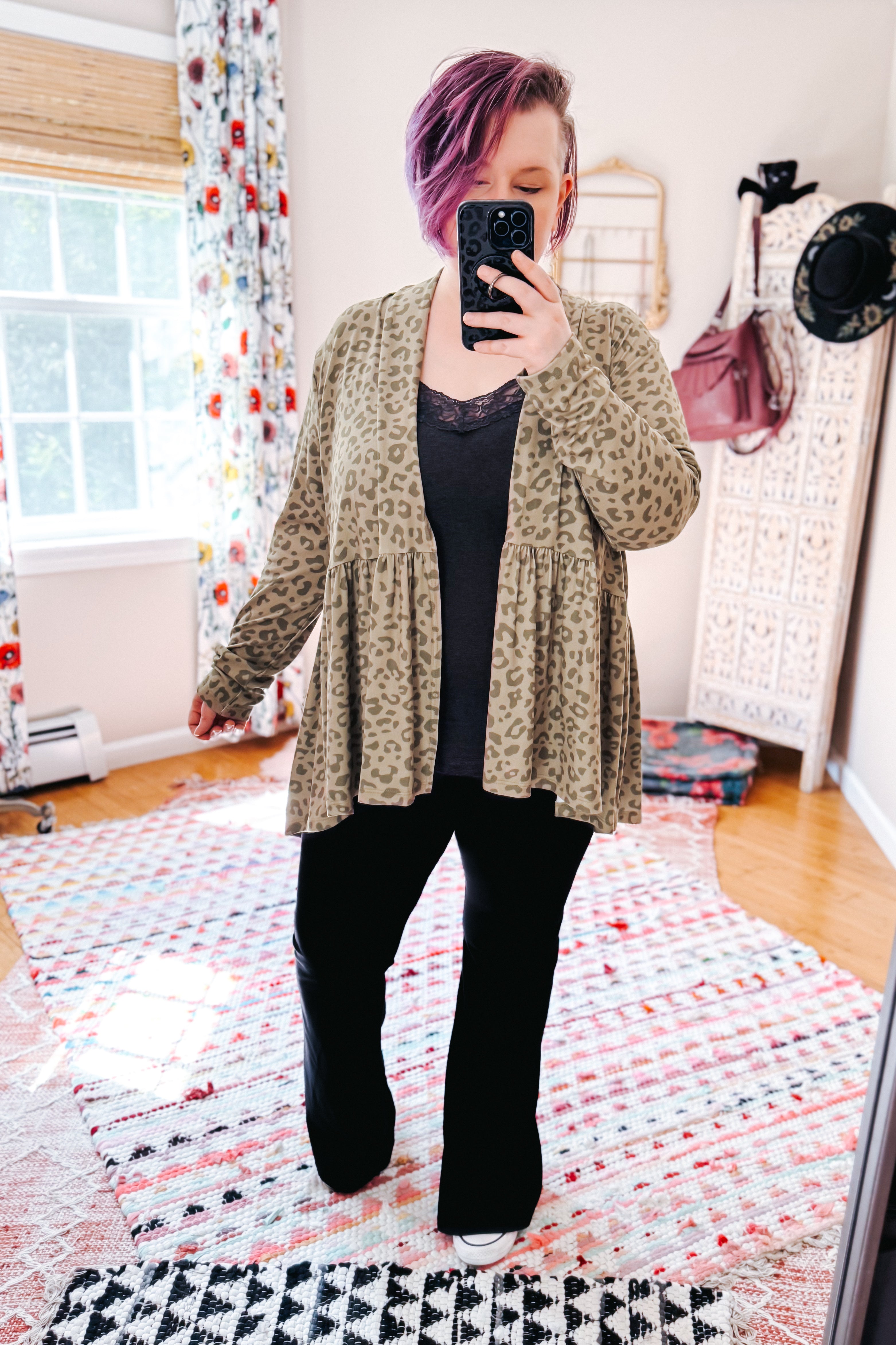 Woman with purple hair wearing green leopard print peplum cardigan over black top in eclectic room with patterned rug and decor