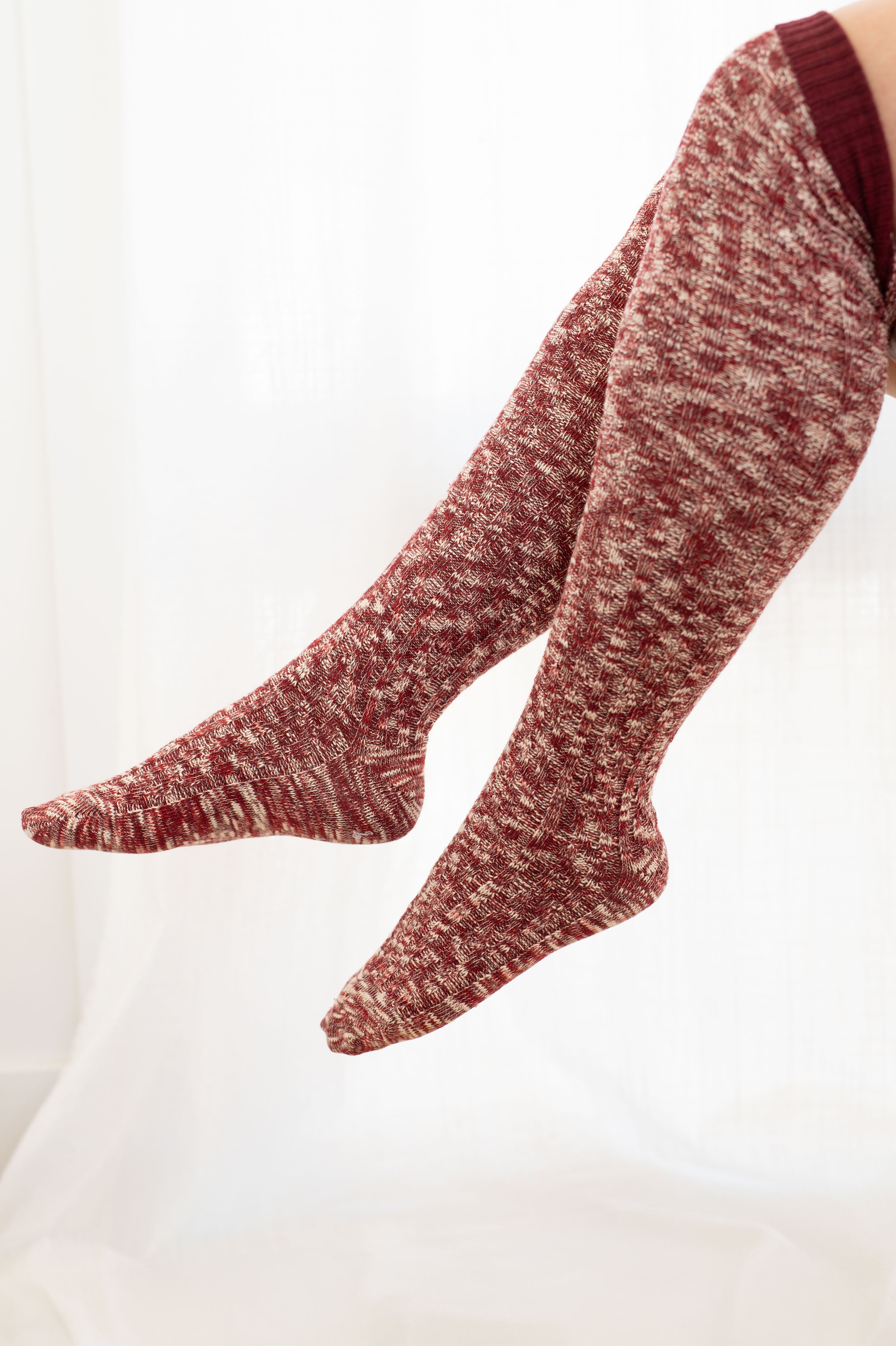Knee-high lounge socks in rich multi red knit pattern on relaxed legs against soft neutral background