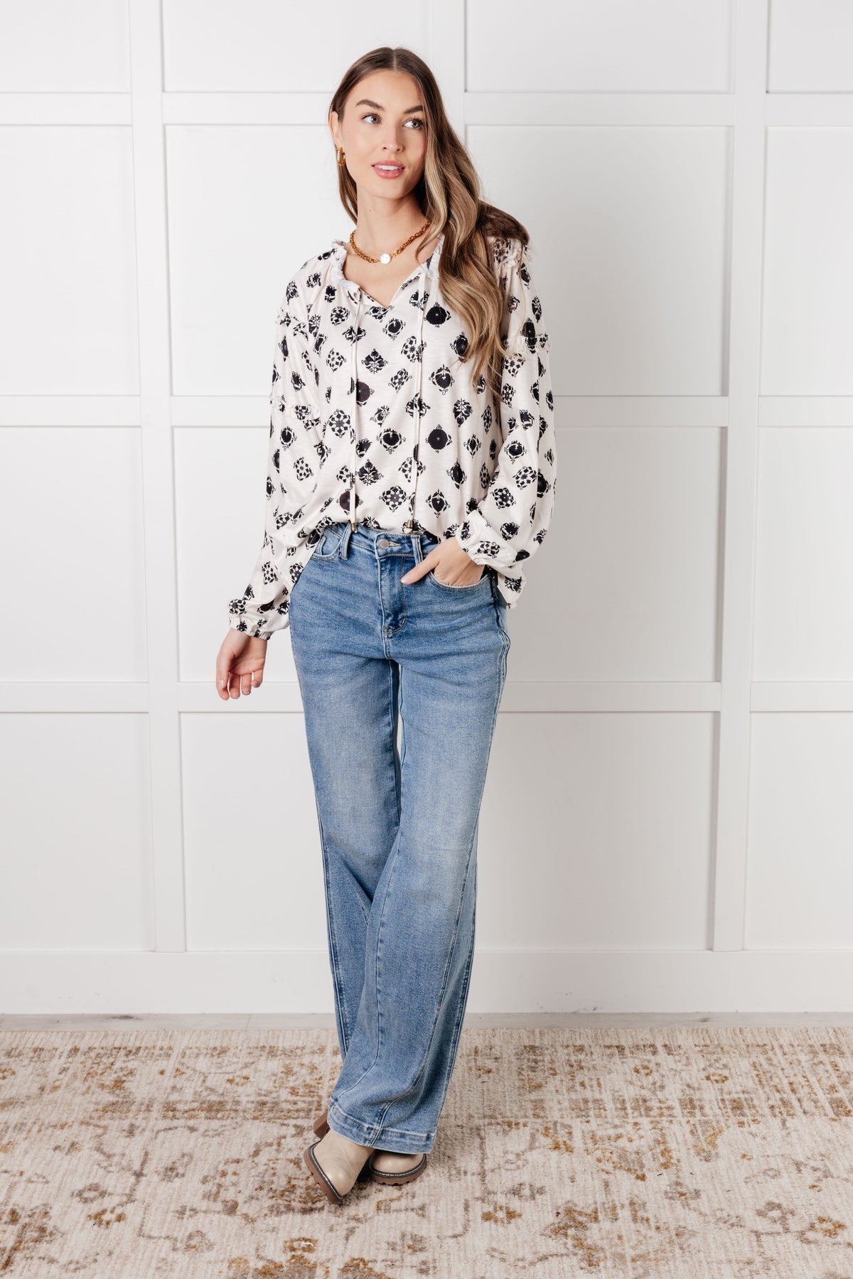 Woman wearing a White floral tile blouse with a split neckline and ruffle details styled with relaxed blue jeans and flats