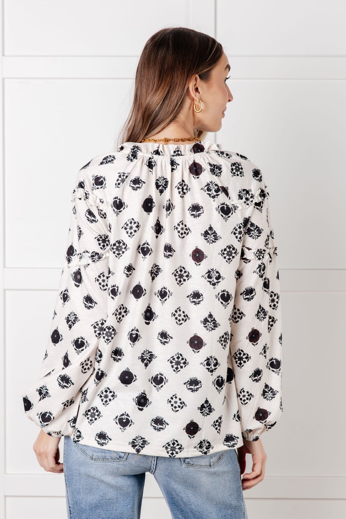 Back view of a woman wearing a white floral tile blouse with gathered neckline and balloon sleeves styled with light wash jeans