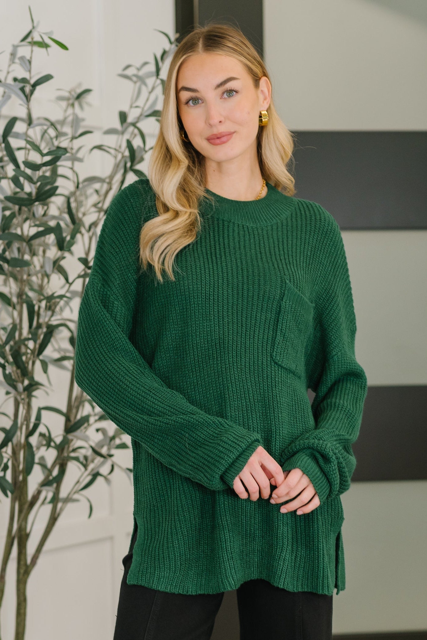 Woman wearing a cozy green textured pullover with a front pocket standing indoors near a leafy plant and window light