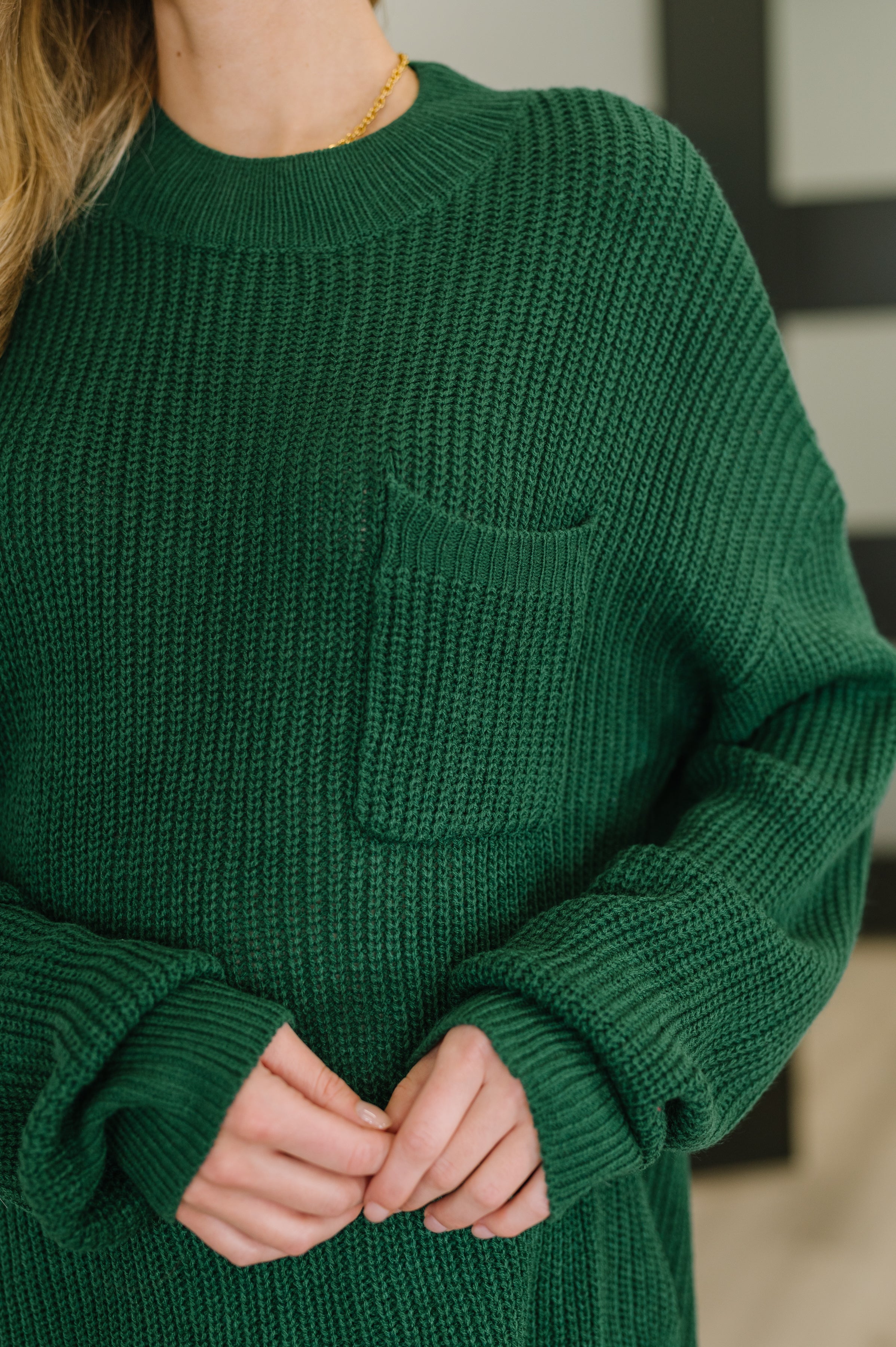 Close-up of a deep green textured pullover with a small chest pocket and cozy ribbed cuffs worn indoors