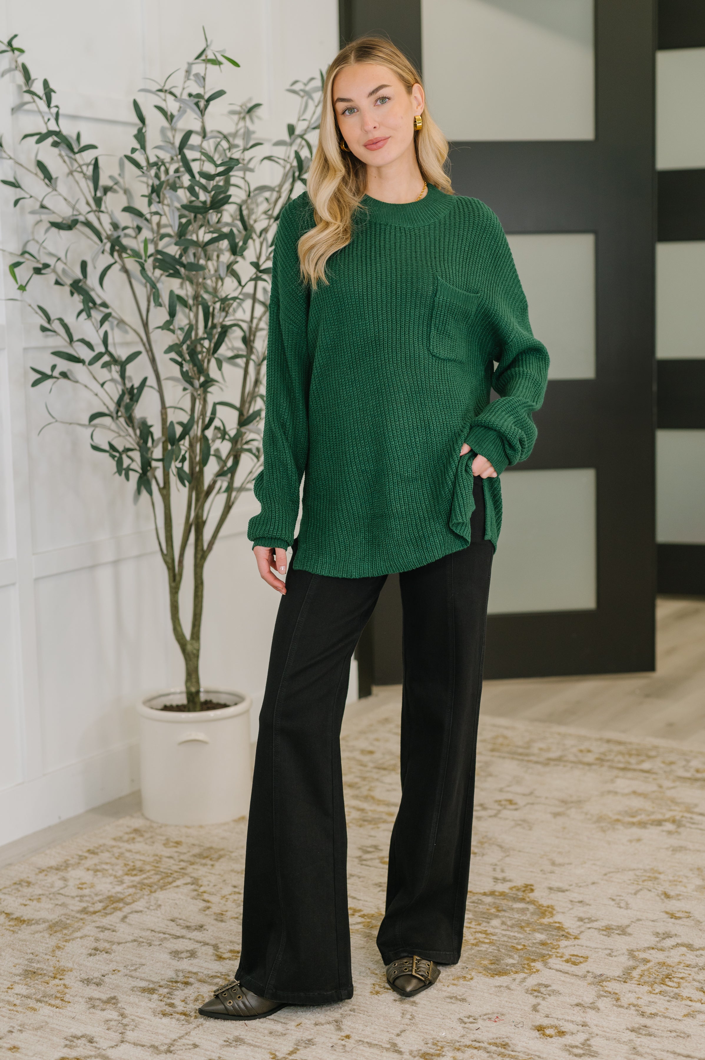 Woman wearing a relaxed green textured pullover with front pocket styled with wide-leg black pants in modern indoor space