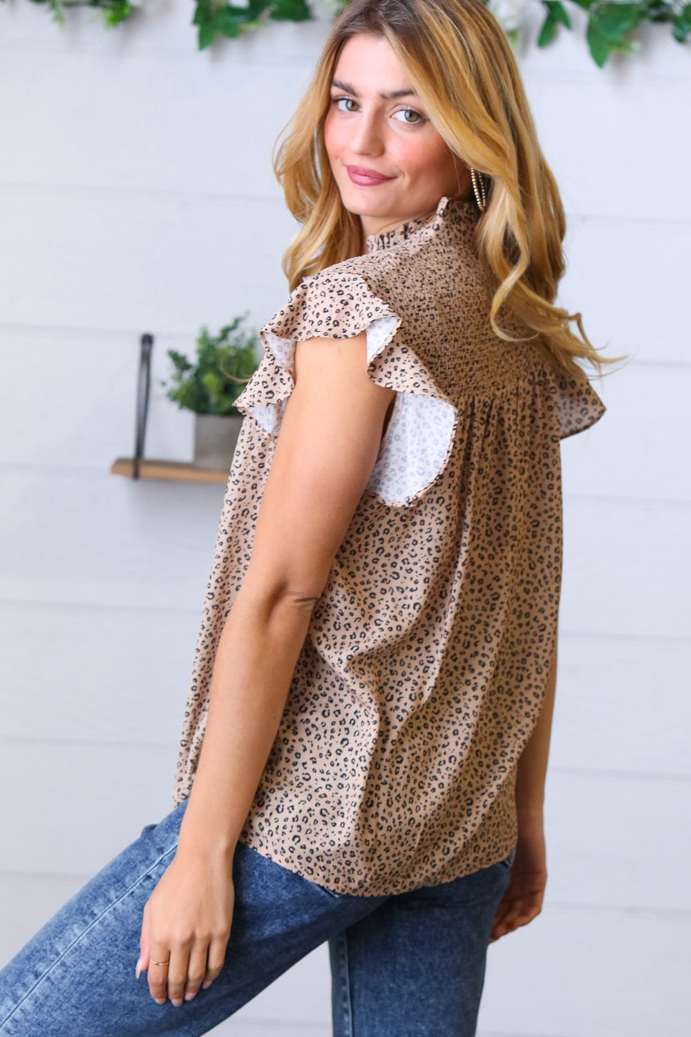 Woman wearing taupe animal print top with ruffled sleeves styled with blue jeans and gold hoop earrings indoors