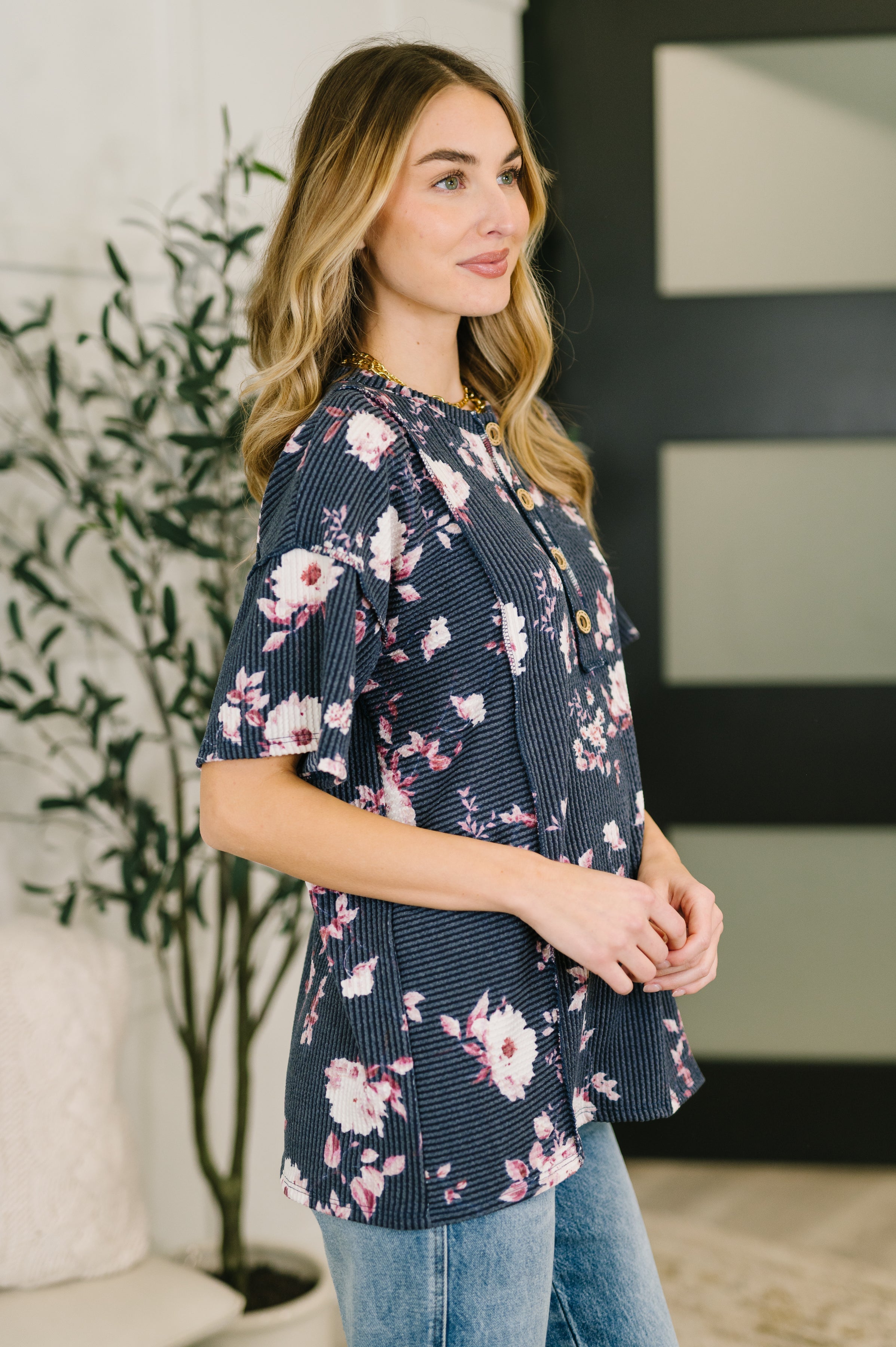 Woman wearing navy floral henley top with wooden buttons paired with light wash jeans standing indoors