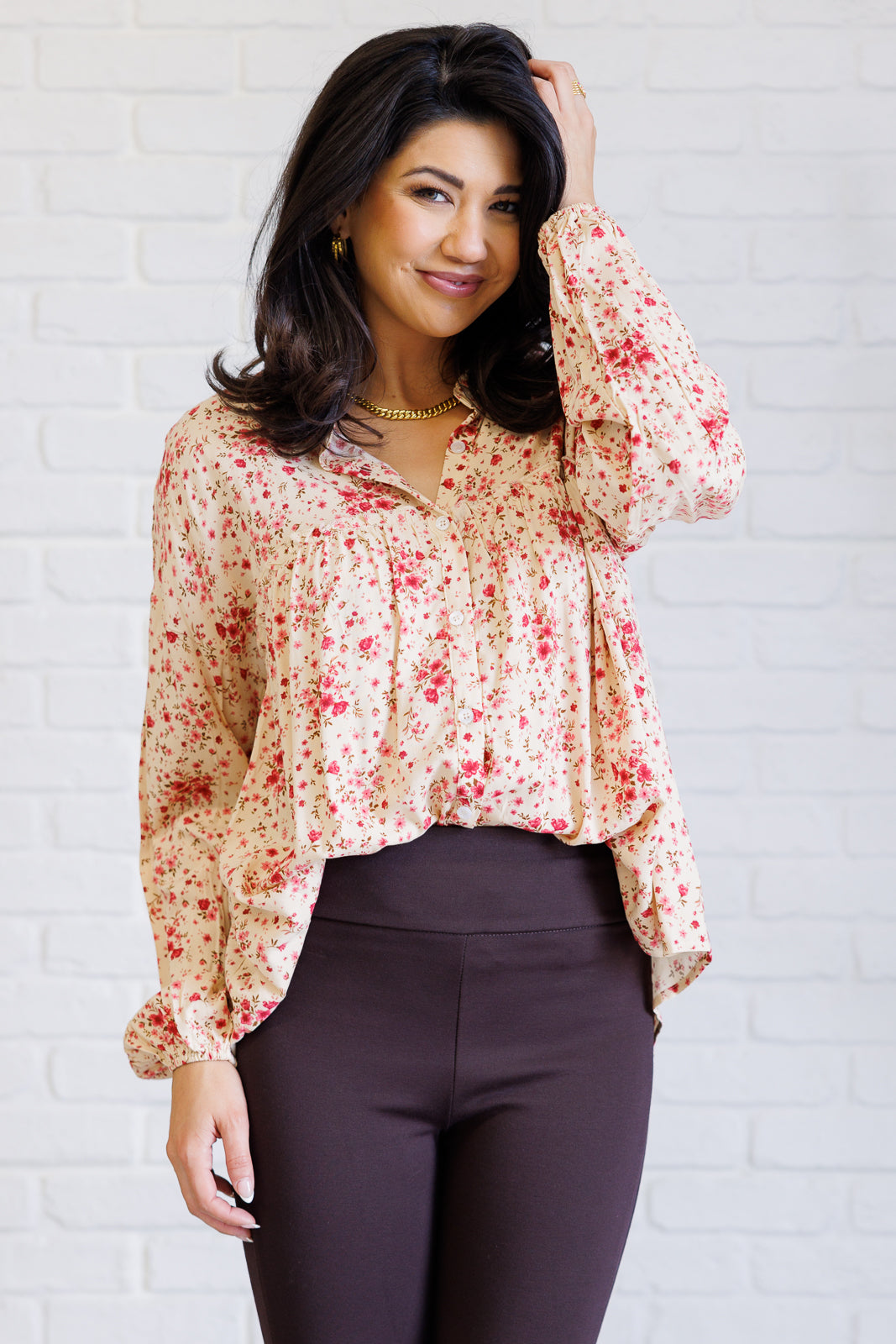 Woman wearing a pink floral button down shirt with a collared neckline and balloon sleeves tucked into dark high waisted pants indoors
