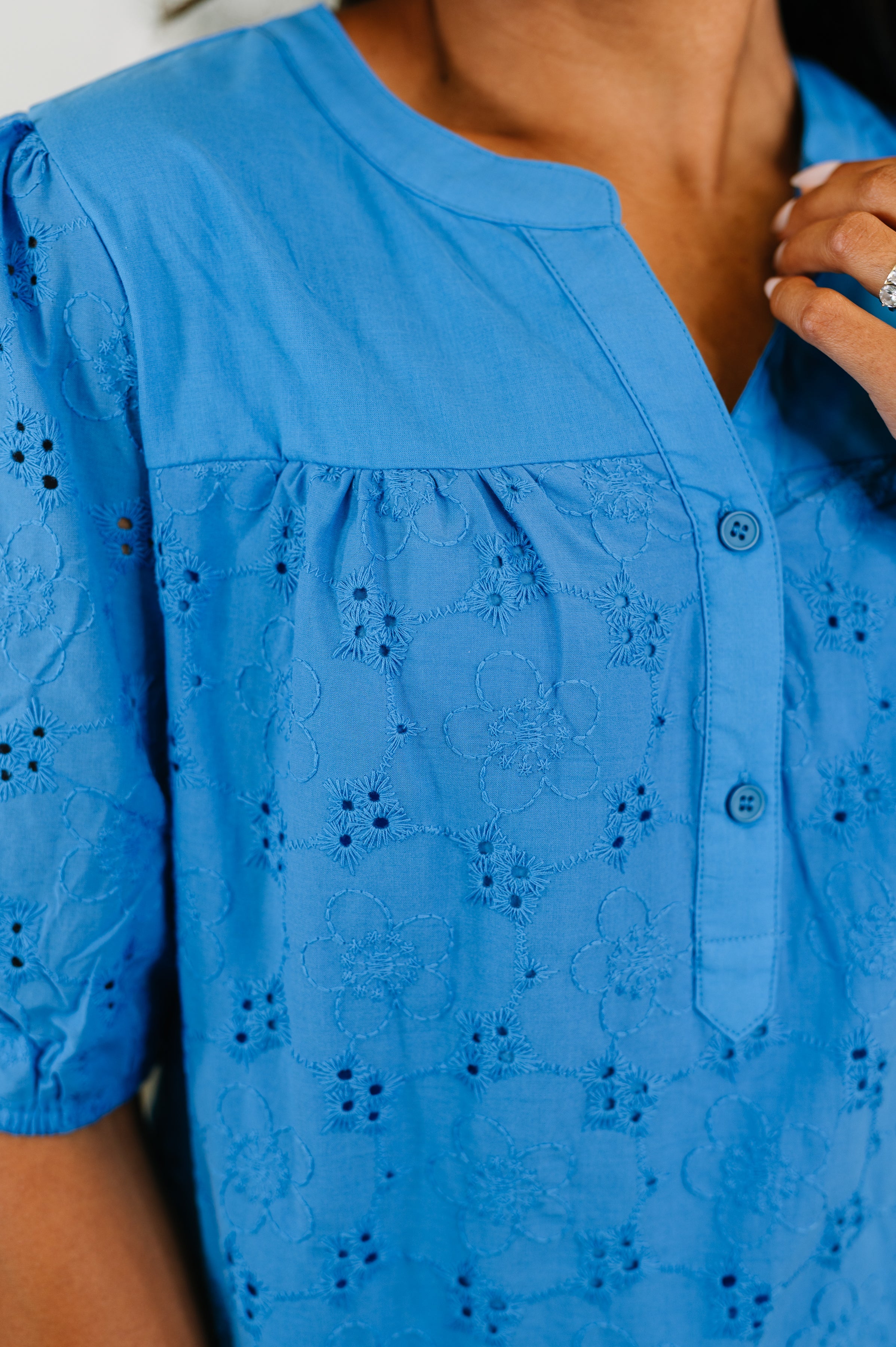 Close-up of blue eyelet blouse with floral embroidery and button detail in a refined, eclectic style