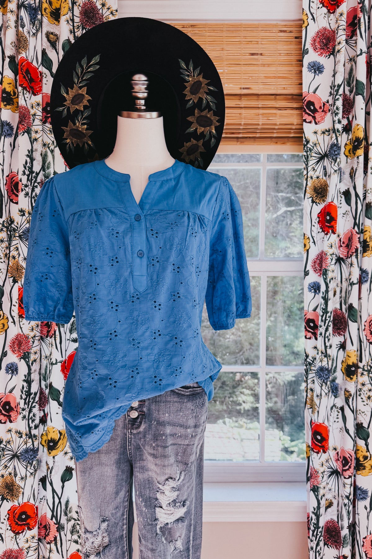Blue eyelet blouse on a mannequin with embroidered floral details split neckline short sleeves and button front styling