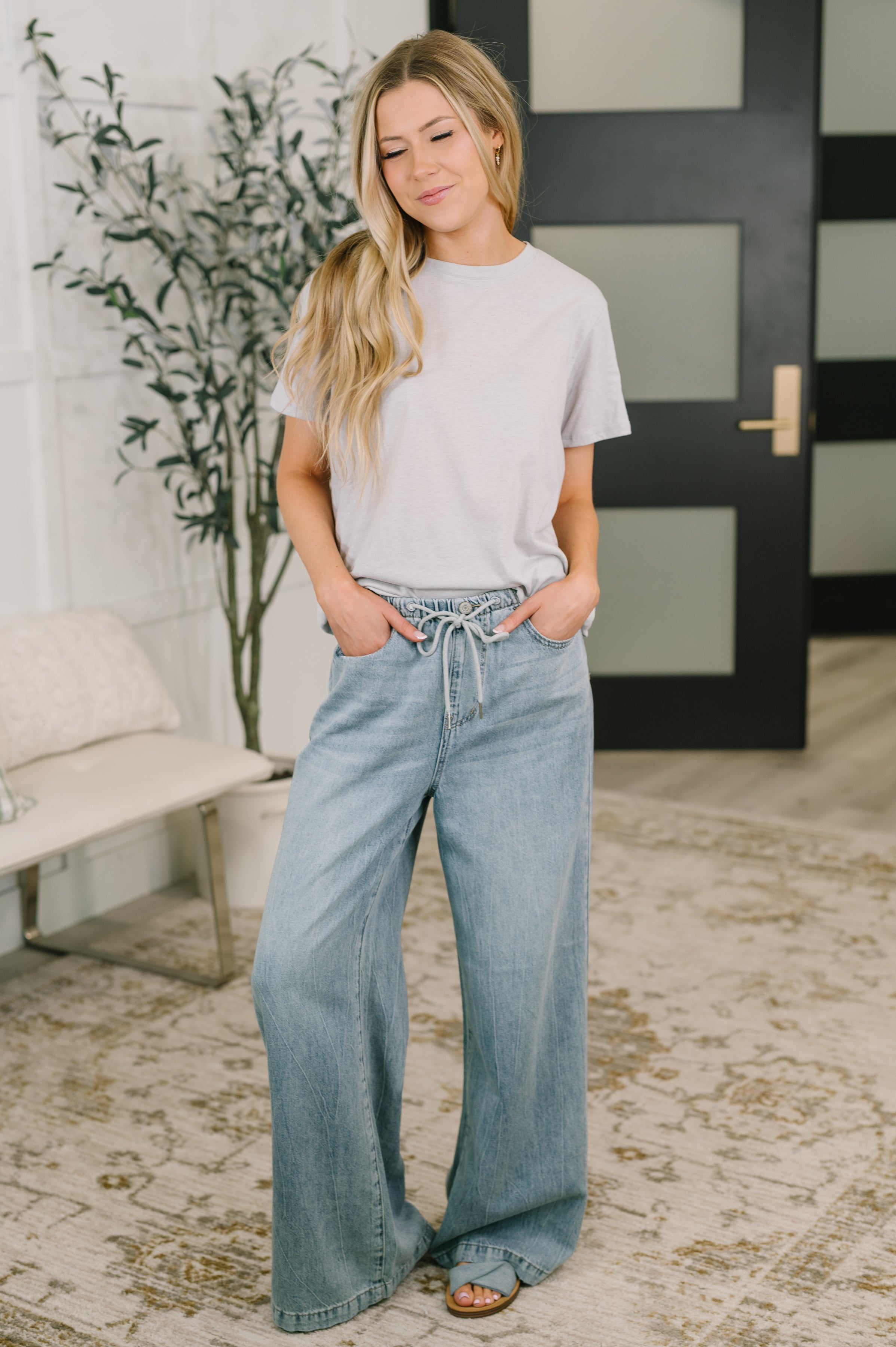 Woman wearing heather grey relaxed fit tee paired with wide-leg light wash jeans in bright indoor room