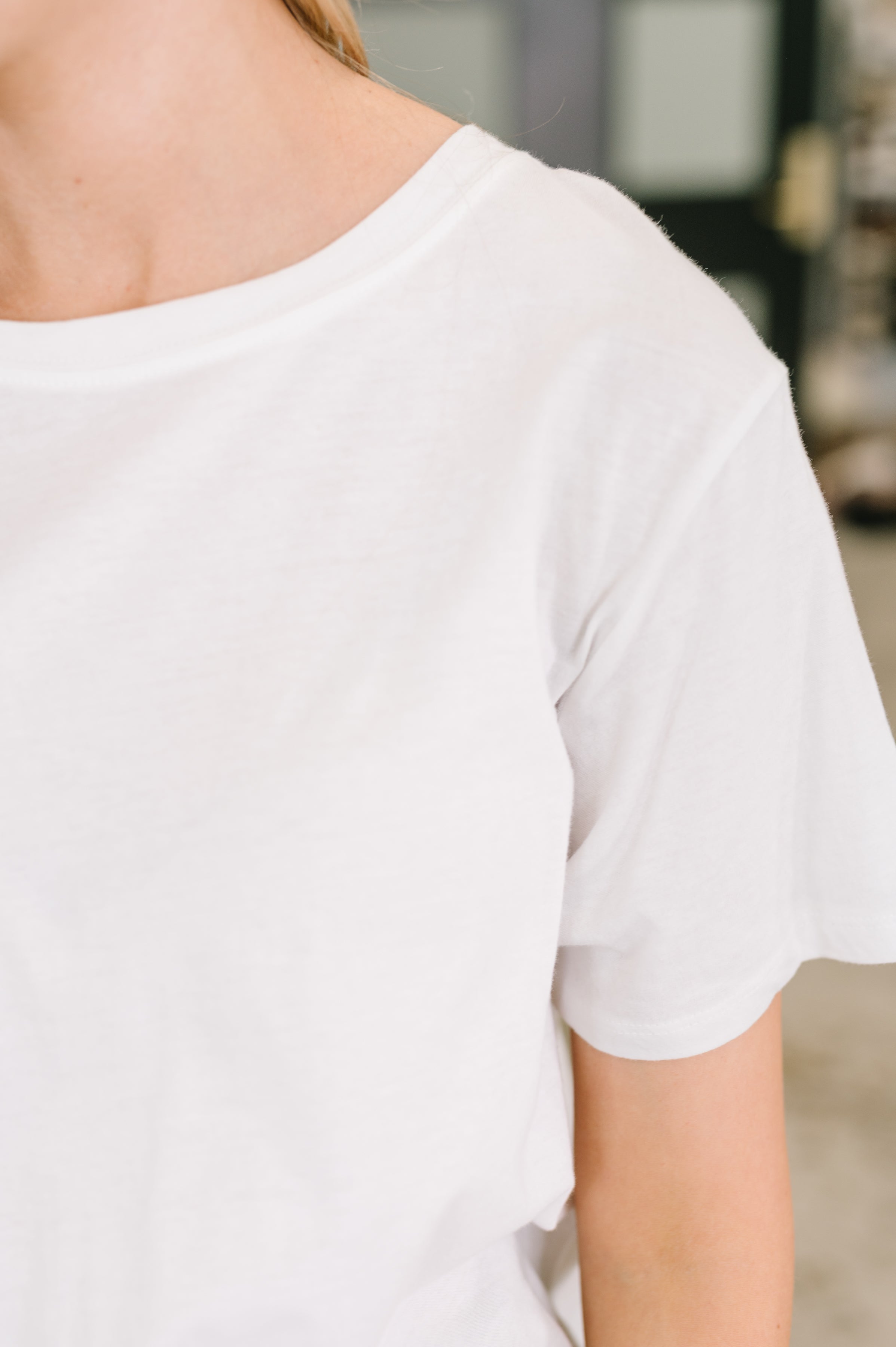 Close-up of person wearing a white relaxed fit tee with short sleeves in a softly lit casual setting