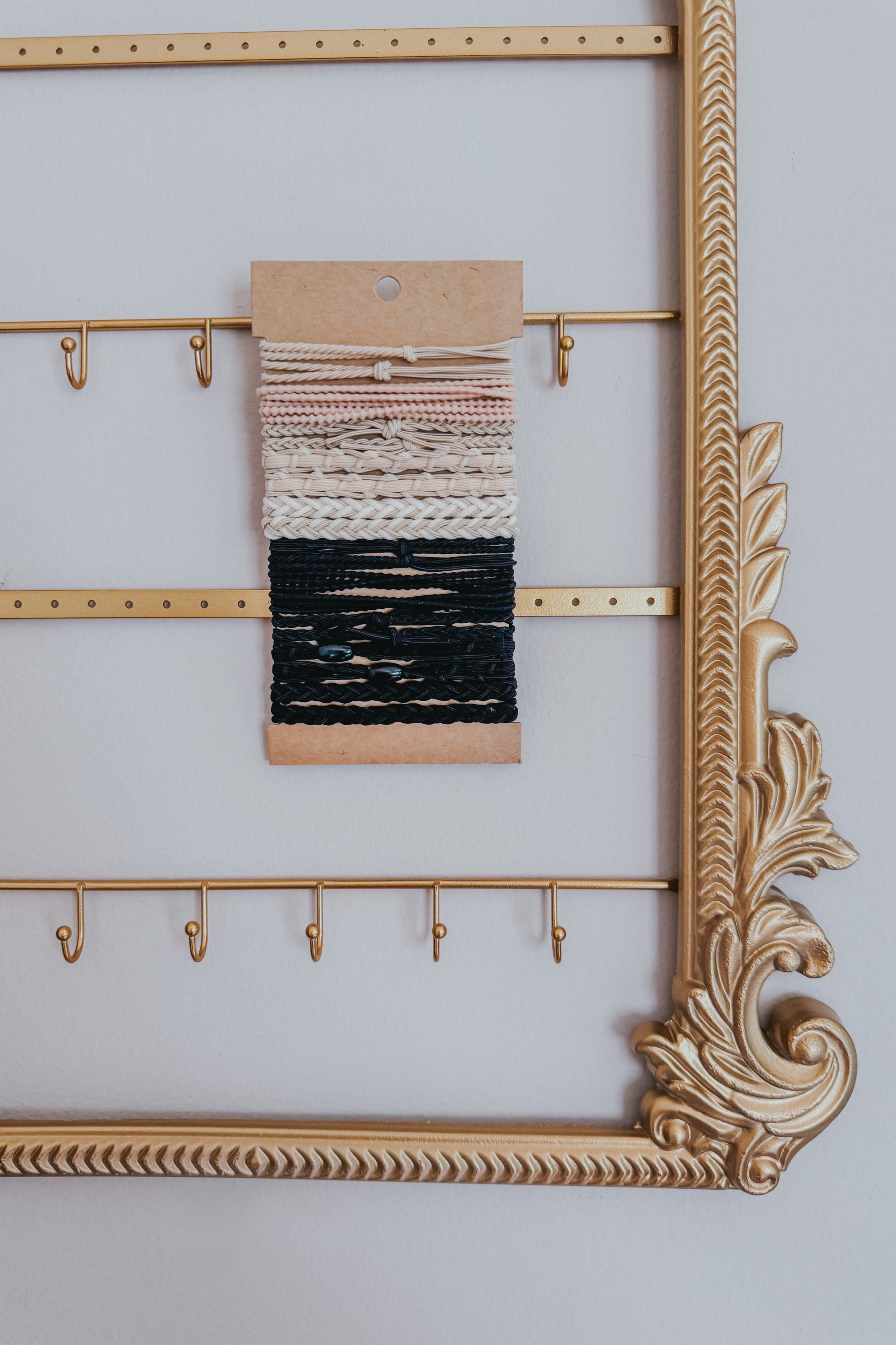Set of cream and black textured stackable hair ties with braided and smooth details displayed on kraft card within ornate gold frame accessory holder