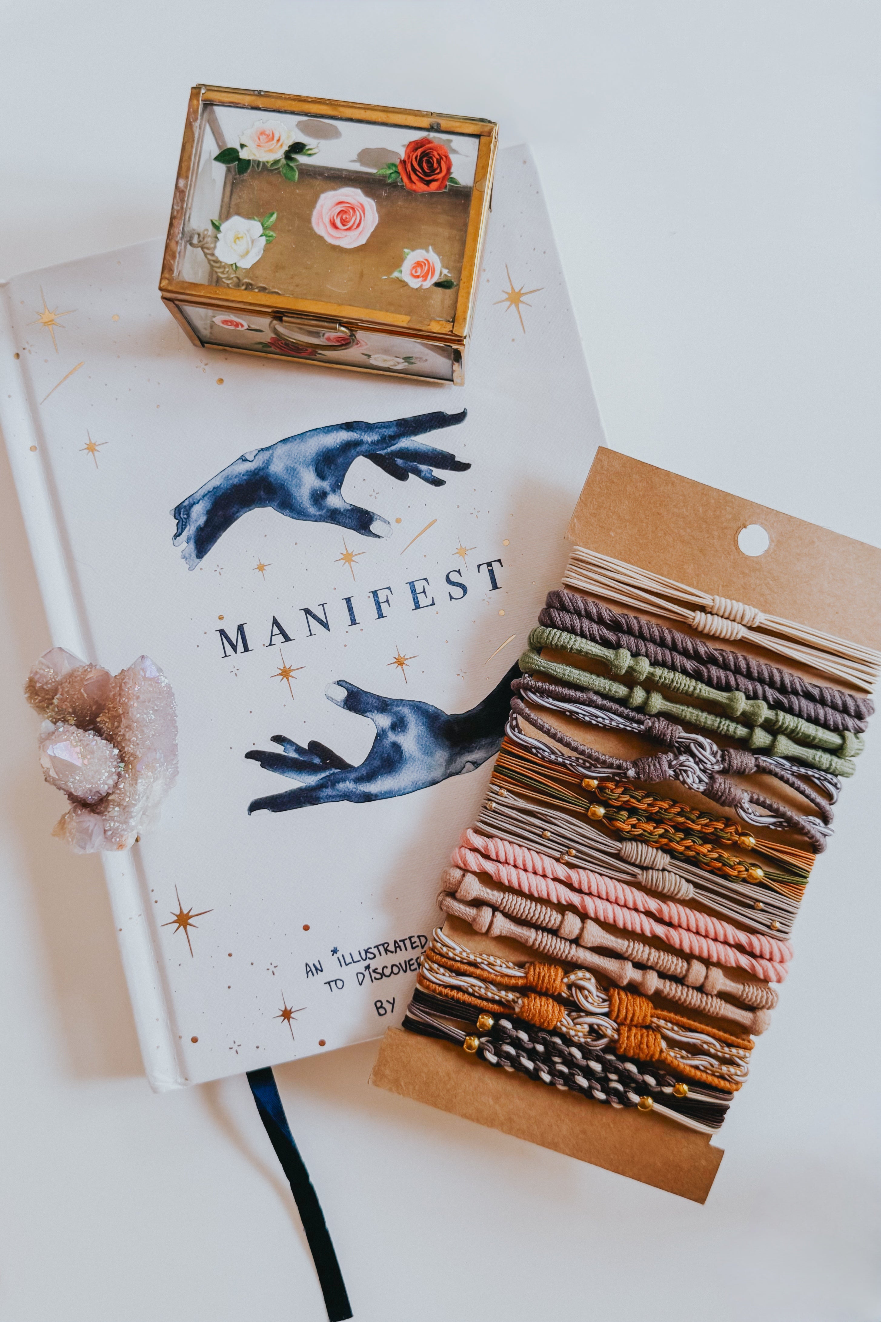 Earth tone knotted and braided hair tie bracelet set displayed on kraft card beside white manifest journal and floral jewelry box