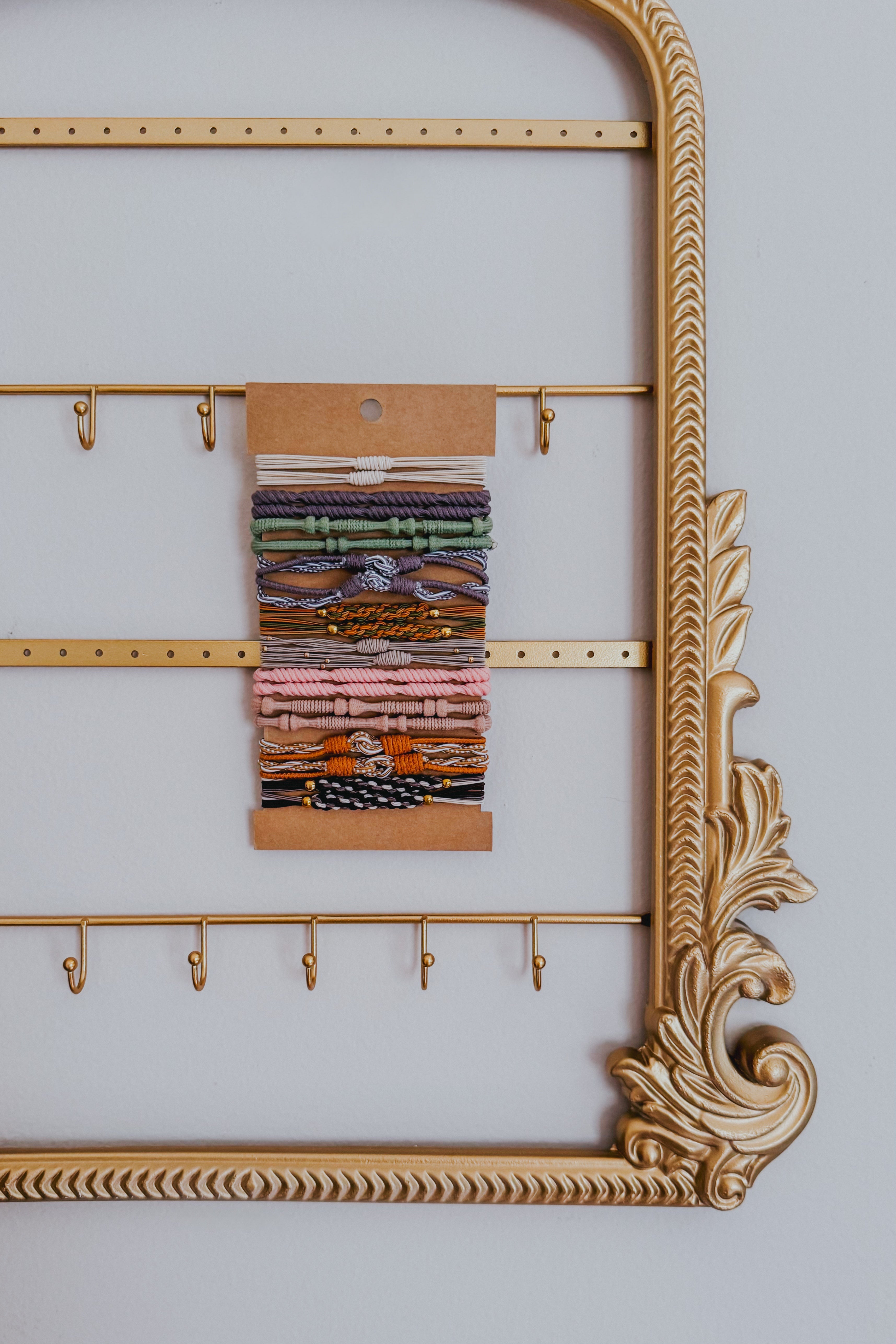 Stack of earth tone stackable hair tie bracelets with varied knotted and braided textures on kraft backing against decorative gold frame