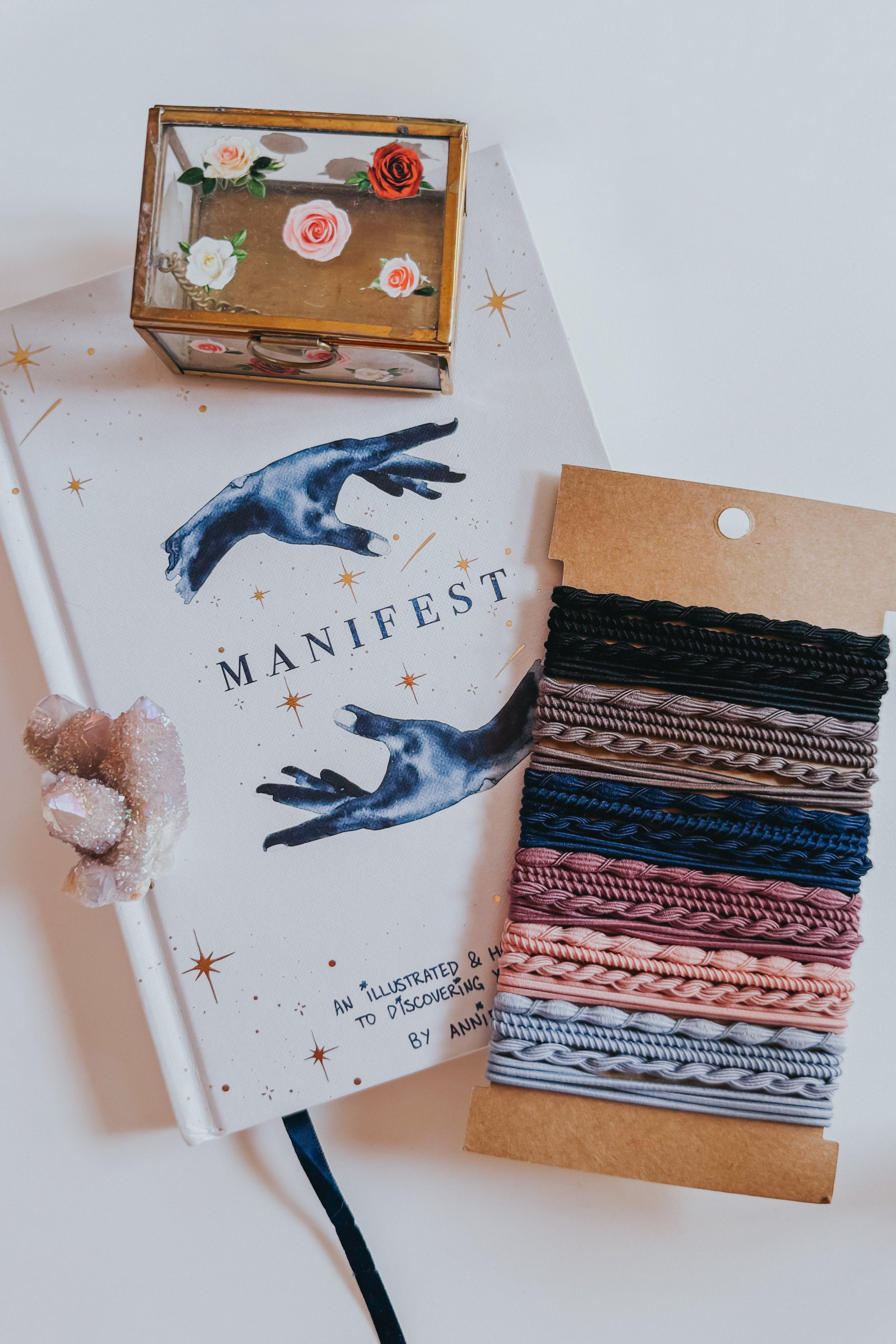 Stack of varied textured hair ties in night sky shades from black to muted pink and blue on kraft card beside a decorative journal and crystal ring holder