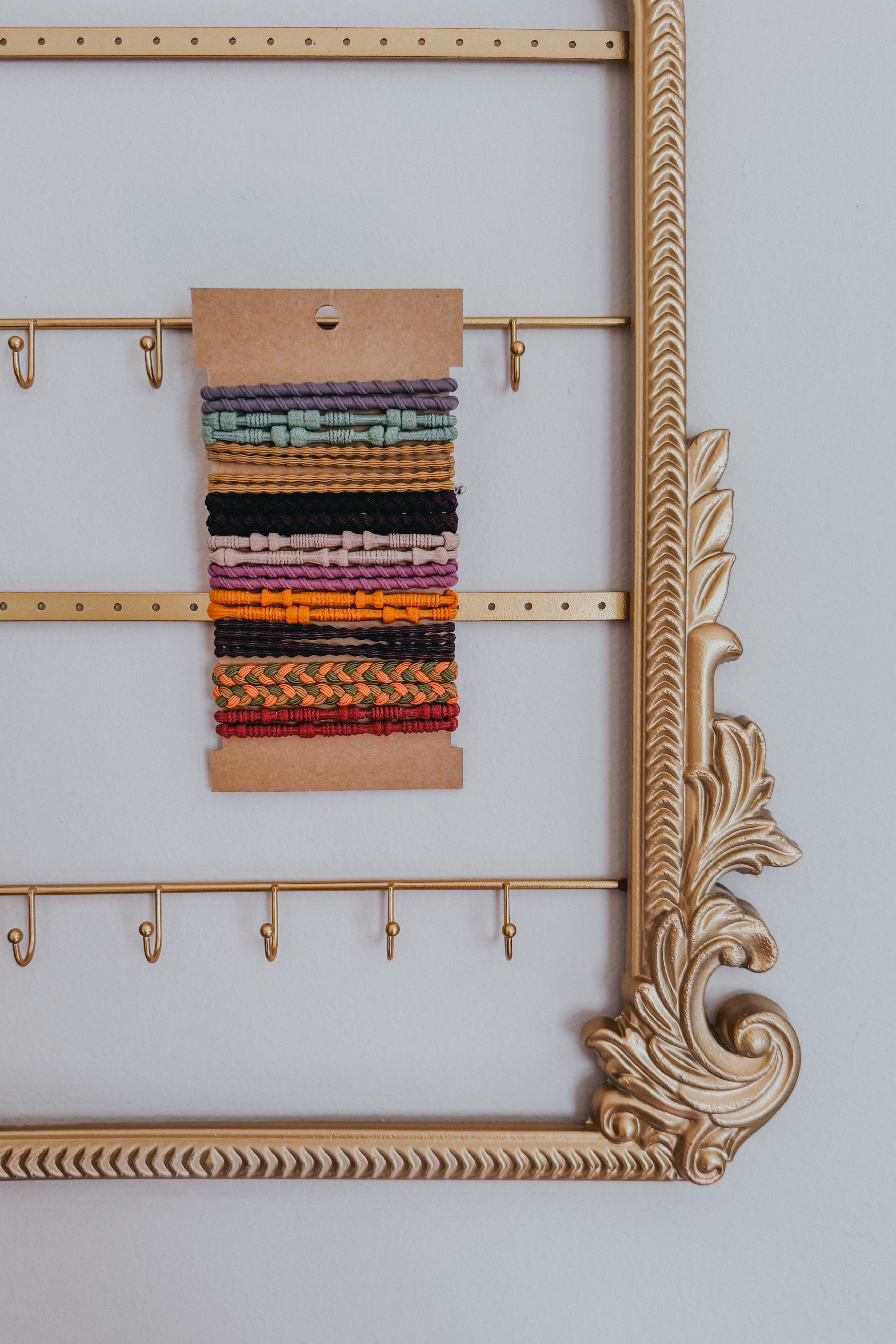 Varied textured stackable hair ties in sunset shades displayed on kraft card within an ornate gold frame