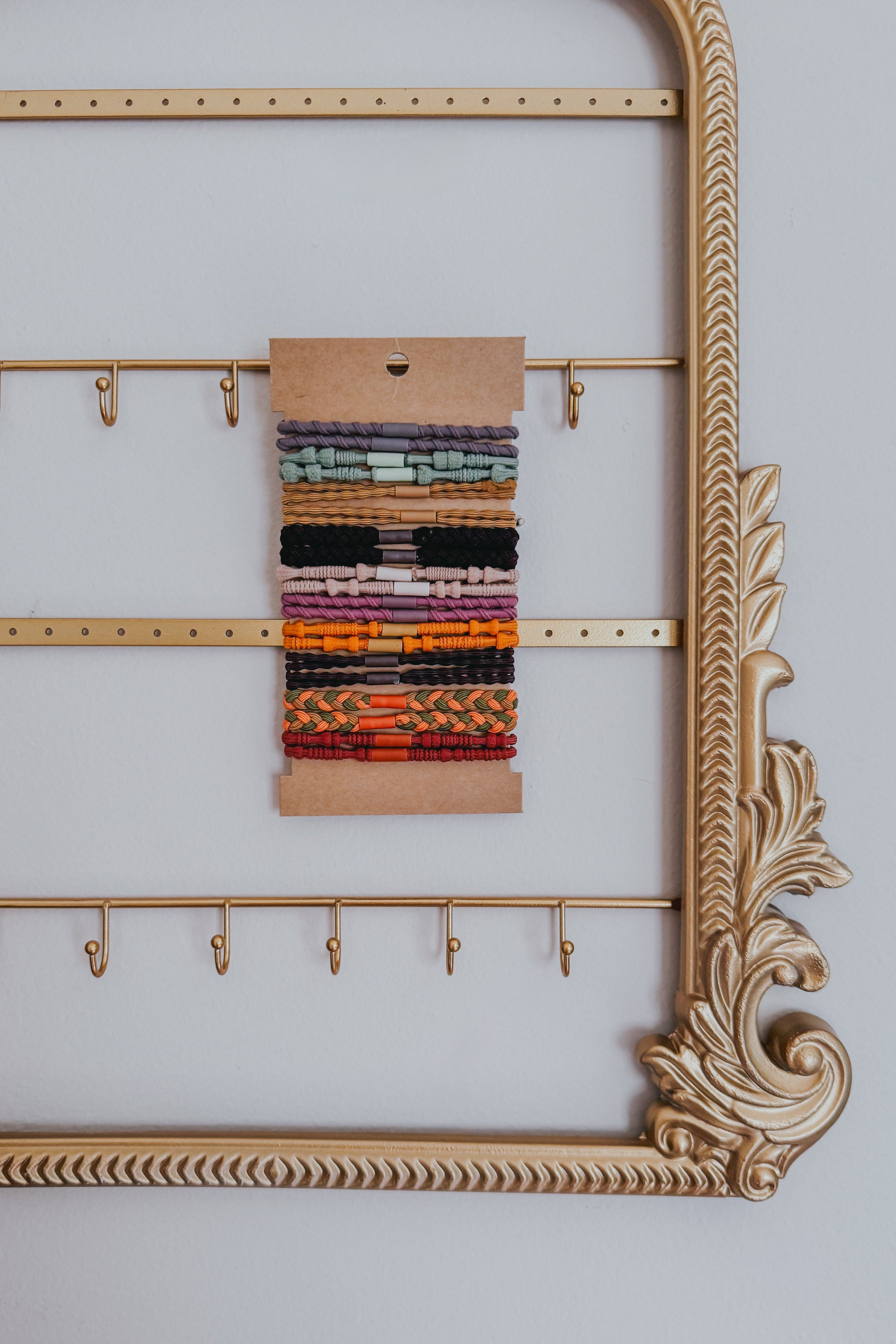 Assortment of artisanal, textured hair ties in warm sunset colors displayed on kraft card within ornate gold frame