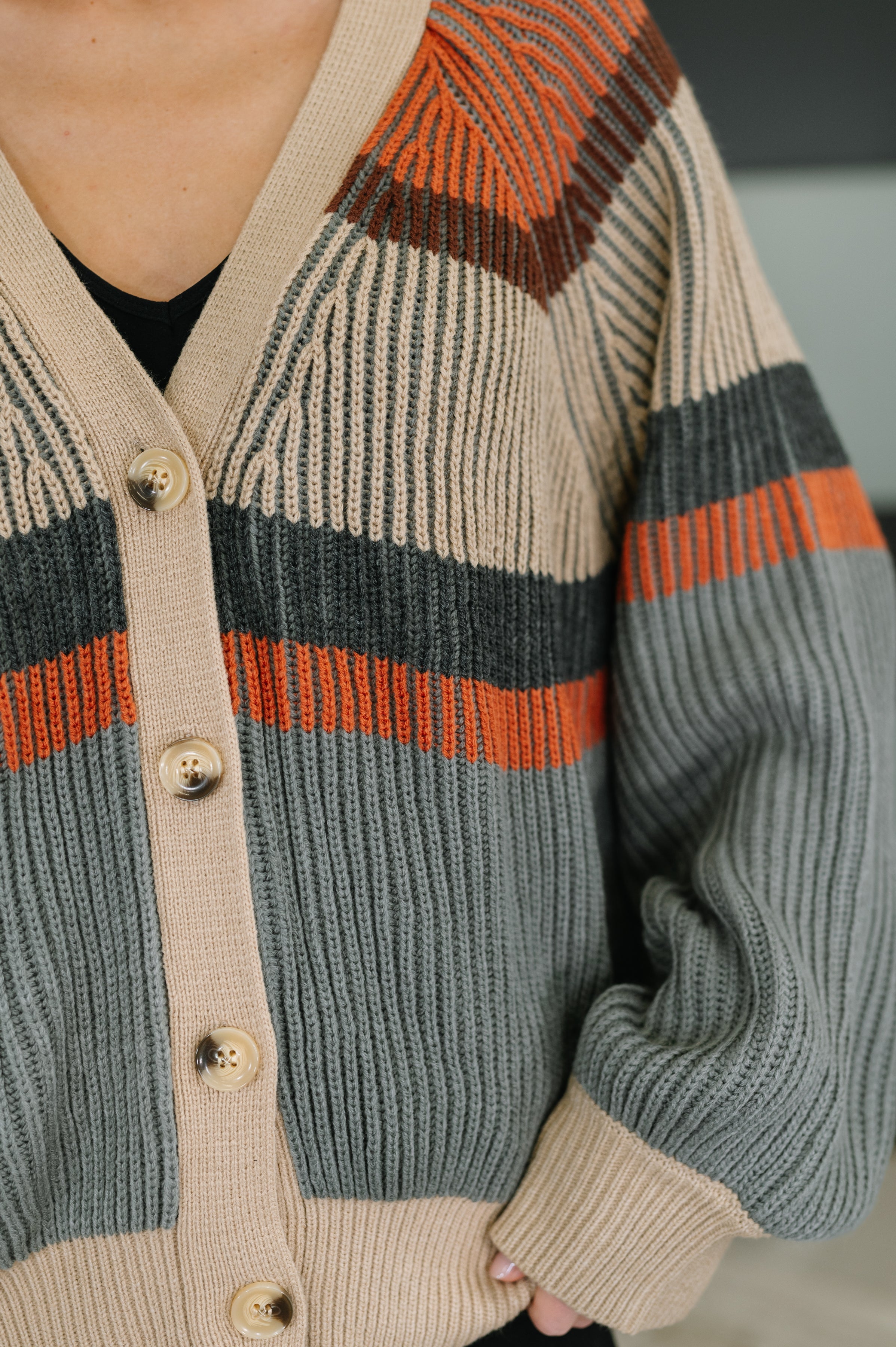 Close-up of knit cardigan in tan, gray, and rust with textured ribbing and button details on relaxed fit sleeve