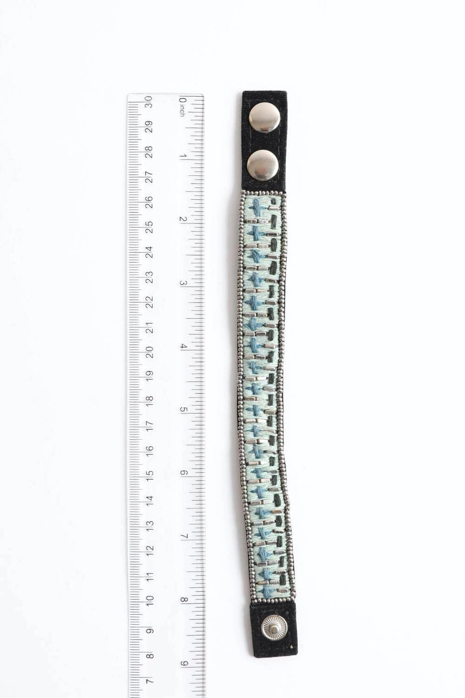 Blue woven velvet snap bracelet with silver fasteners shown next to clear plastic ruler on white background