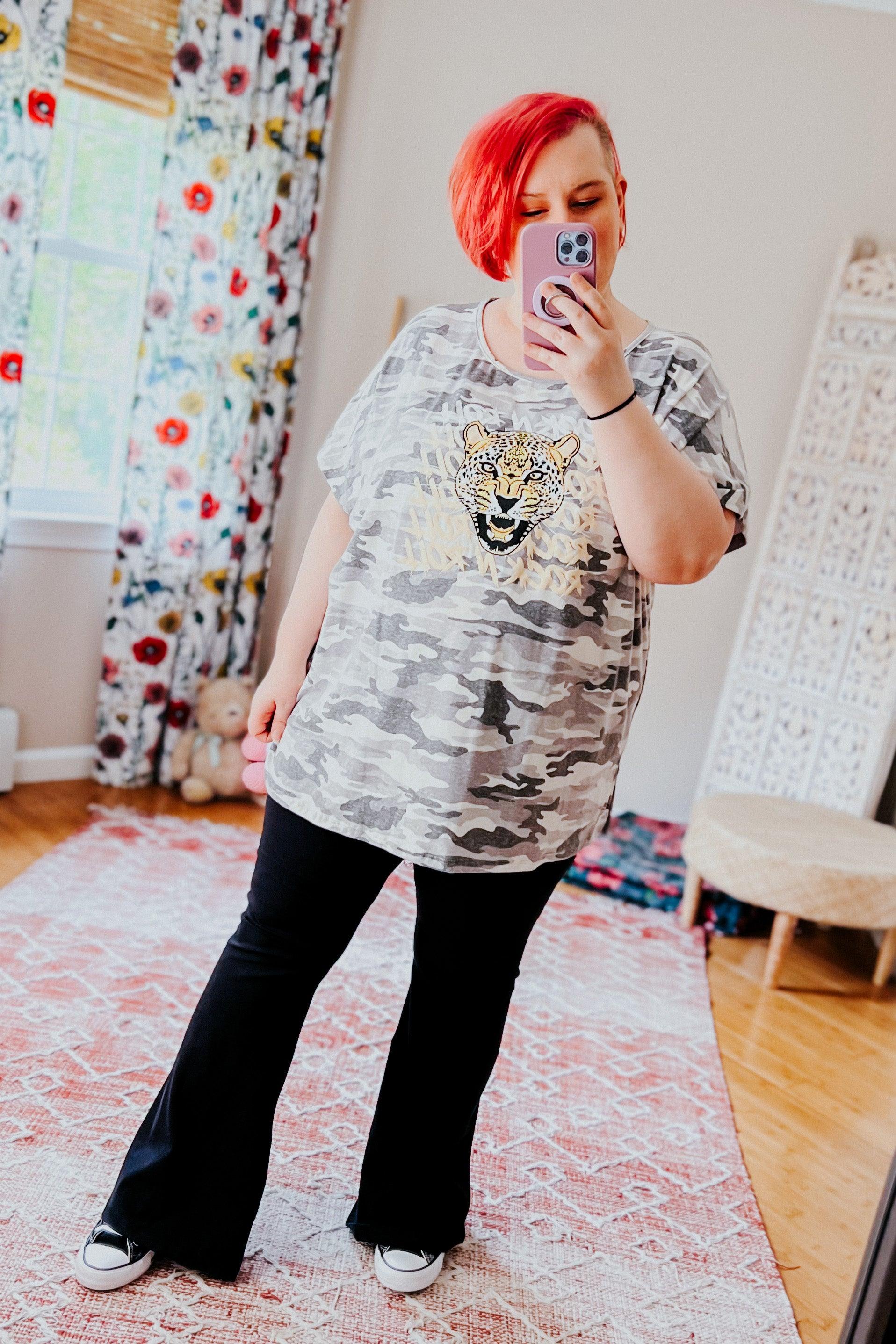 Plus size model with red hair wearing a grey camo Rock N Roll Leopard Tee and black flared pants in cozy room