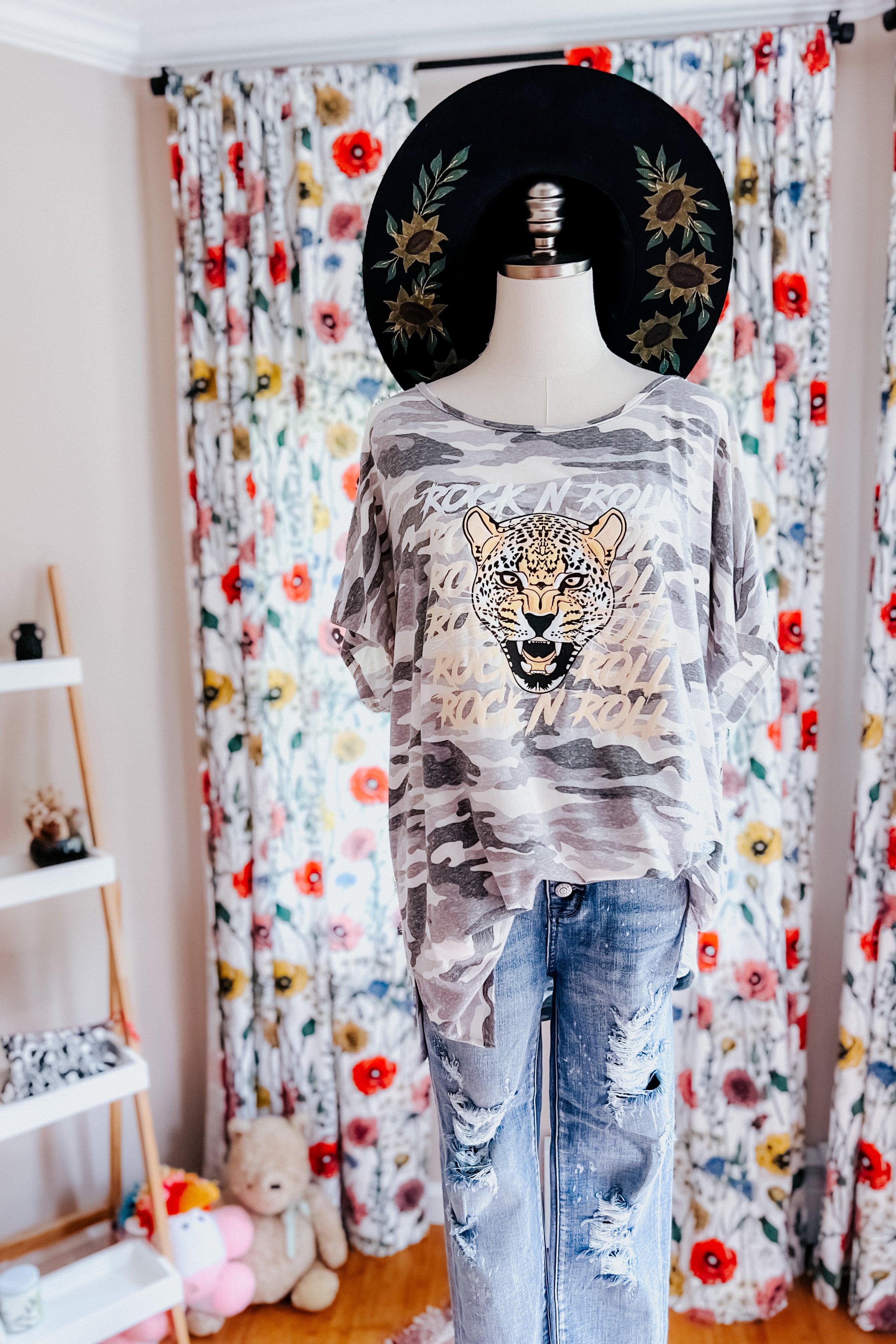 Grey camo tee with bold leopard face and repeating rock n roll text paired with distressed light denim jeans on mannequin
