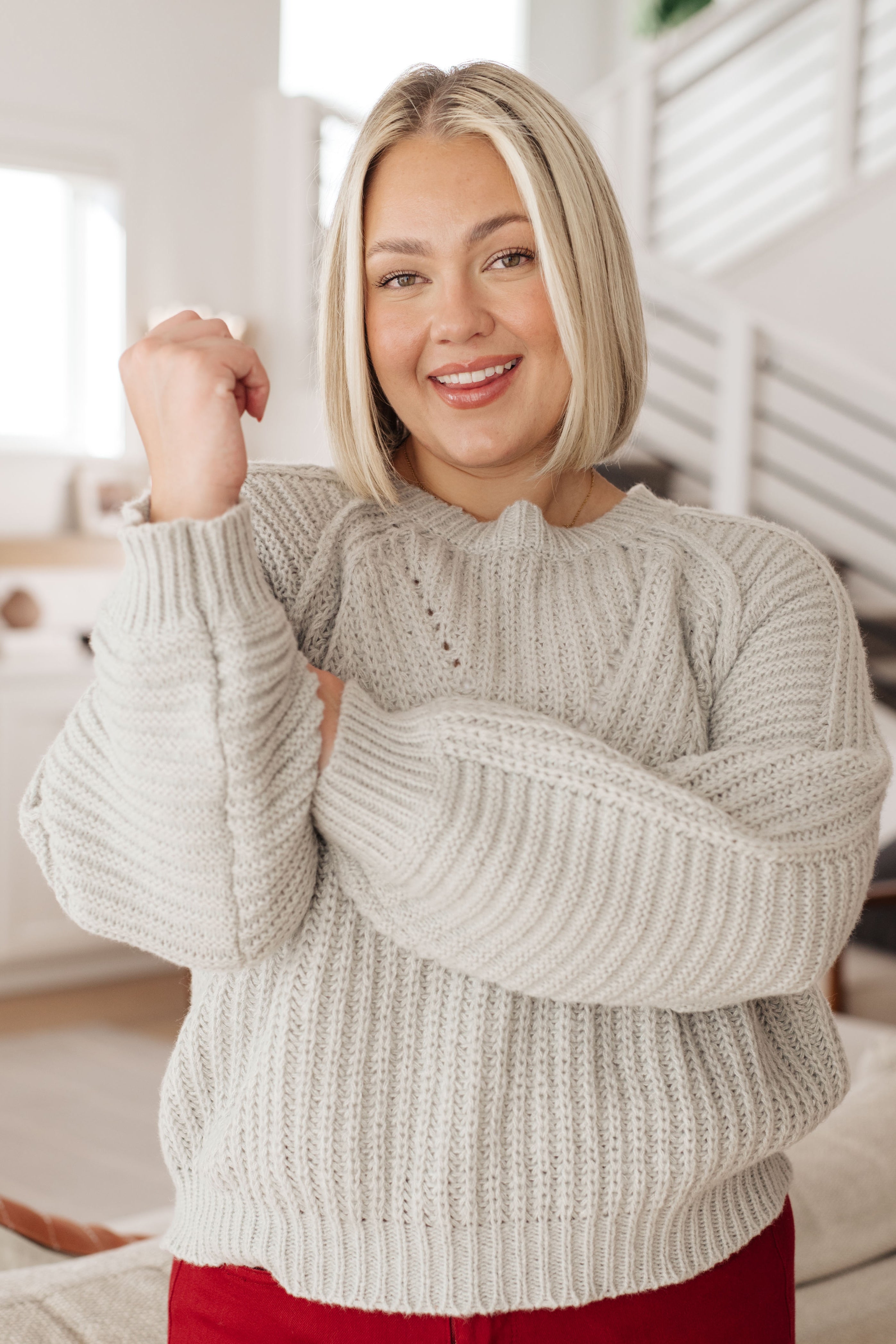 Smiling woman wearing grey balloon sleeve sweater in cozy indoor setting with modern minimalist background