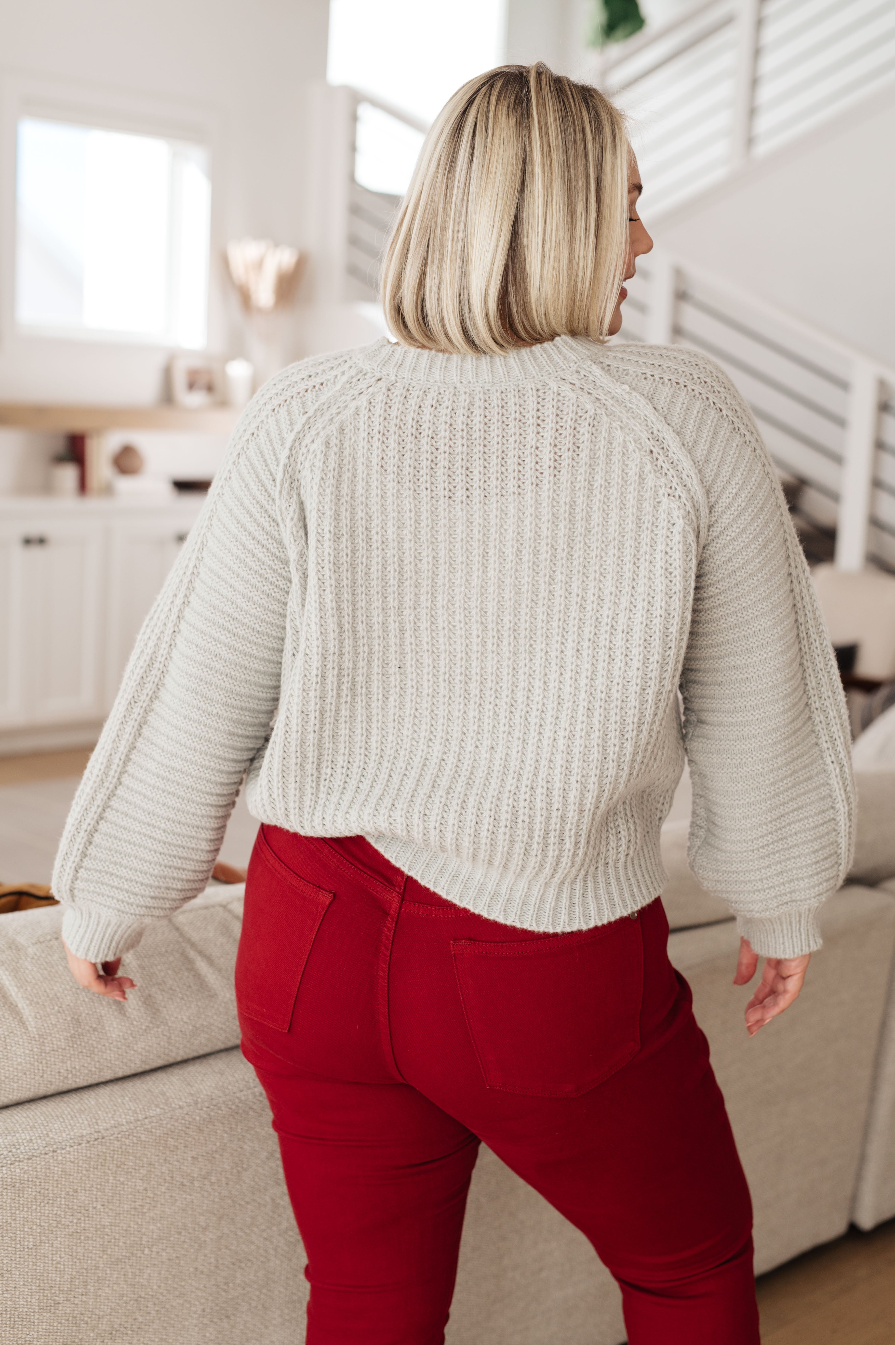 Woman with blonde bob wearing cream balloon sleeve sweater paired with red pants in cozy living room setting