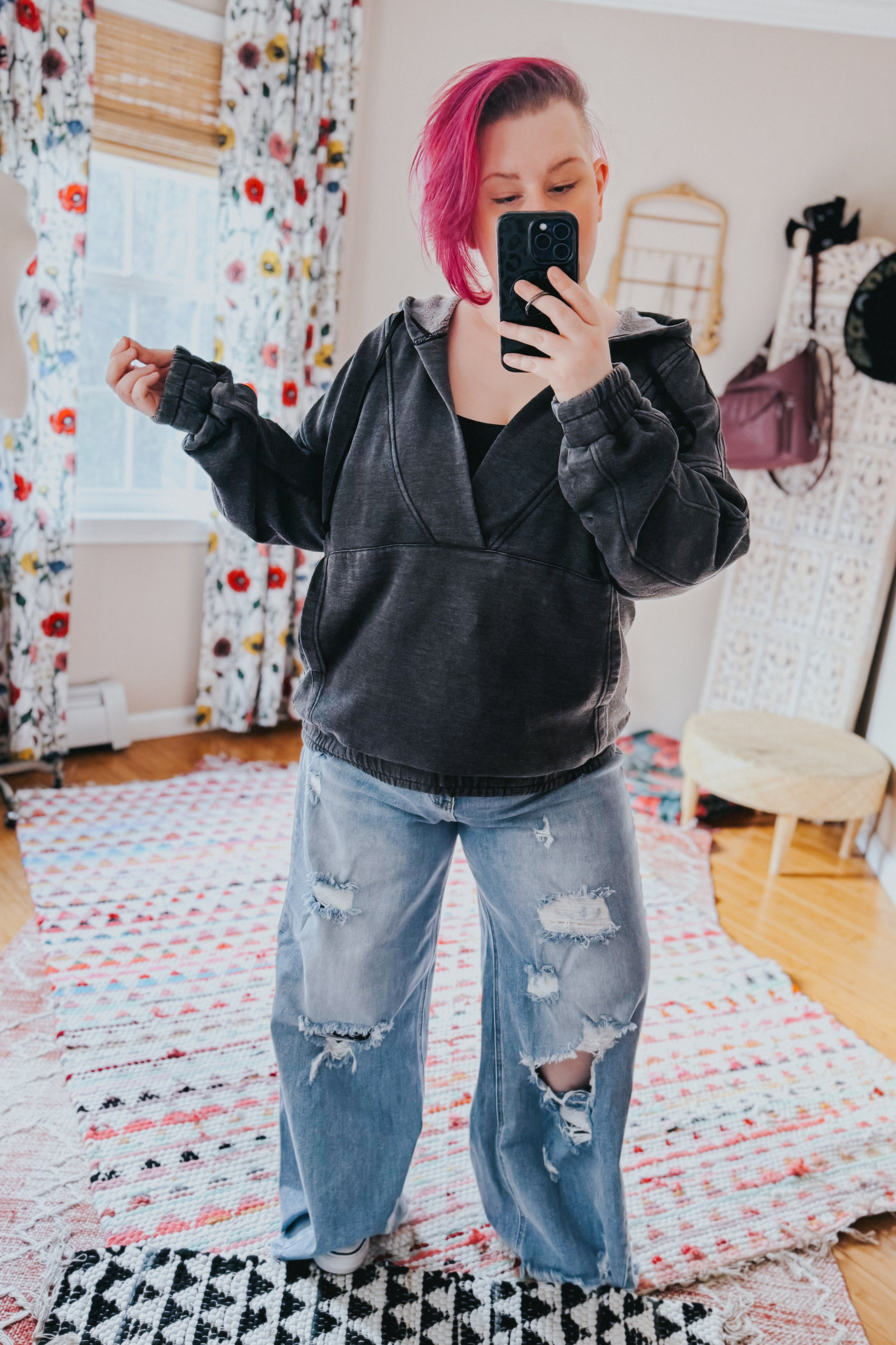 Woman with pink hair wearing charcoal acid wash hoodie and ripped wide-leg jeans taking a selfie indoors