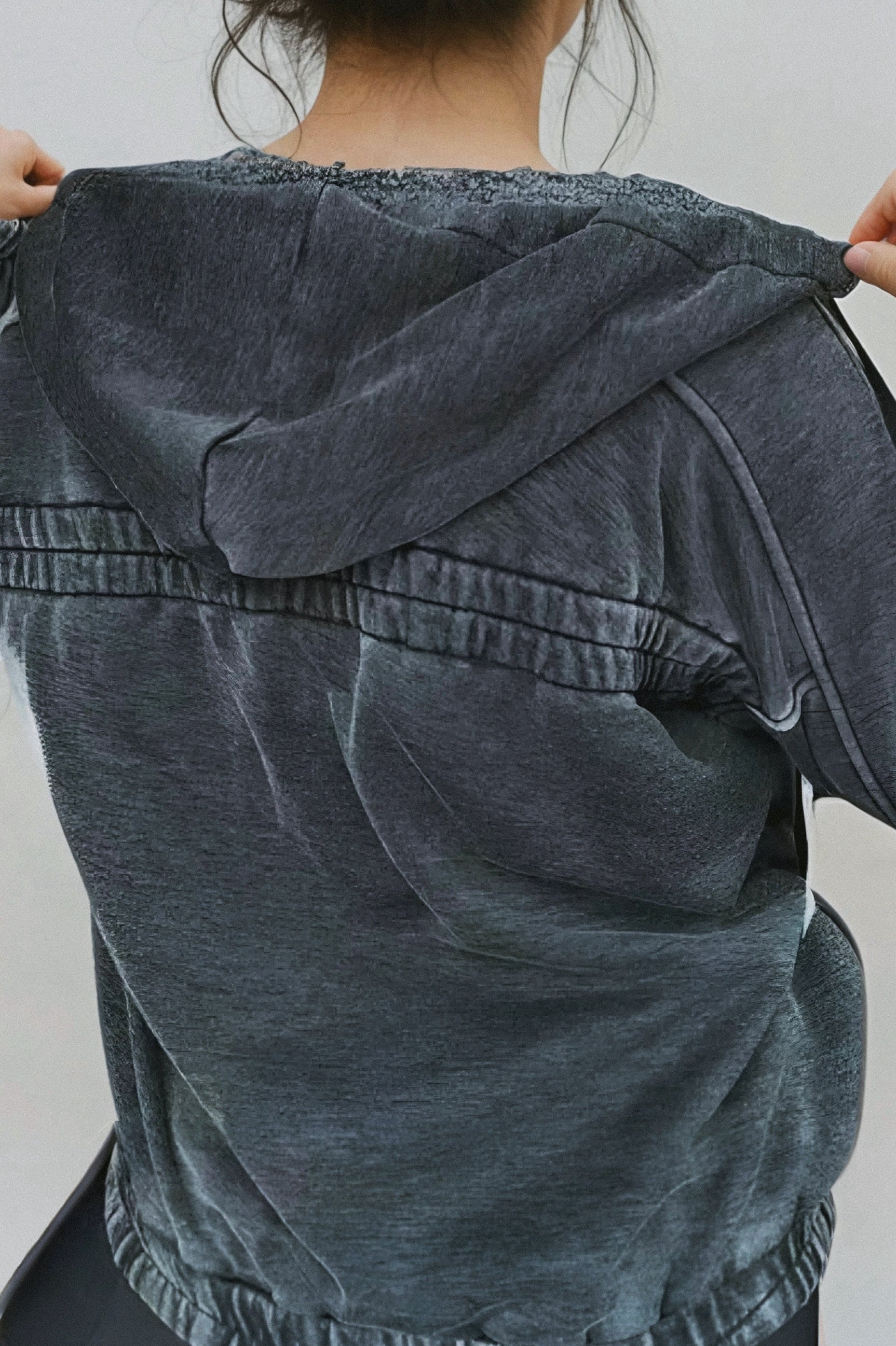 Woman wearing oversized charcoal acid wash hoodie with hood up, shown from the back in casual setting