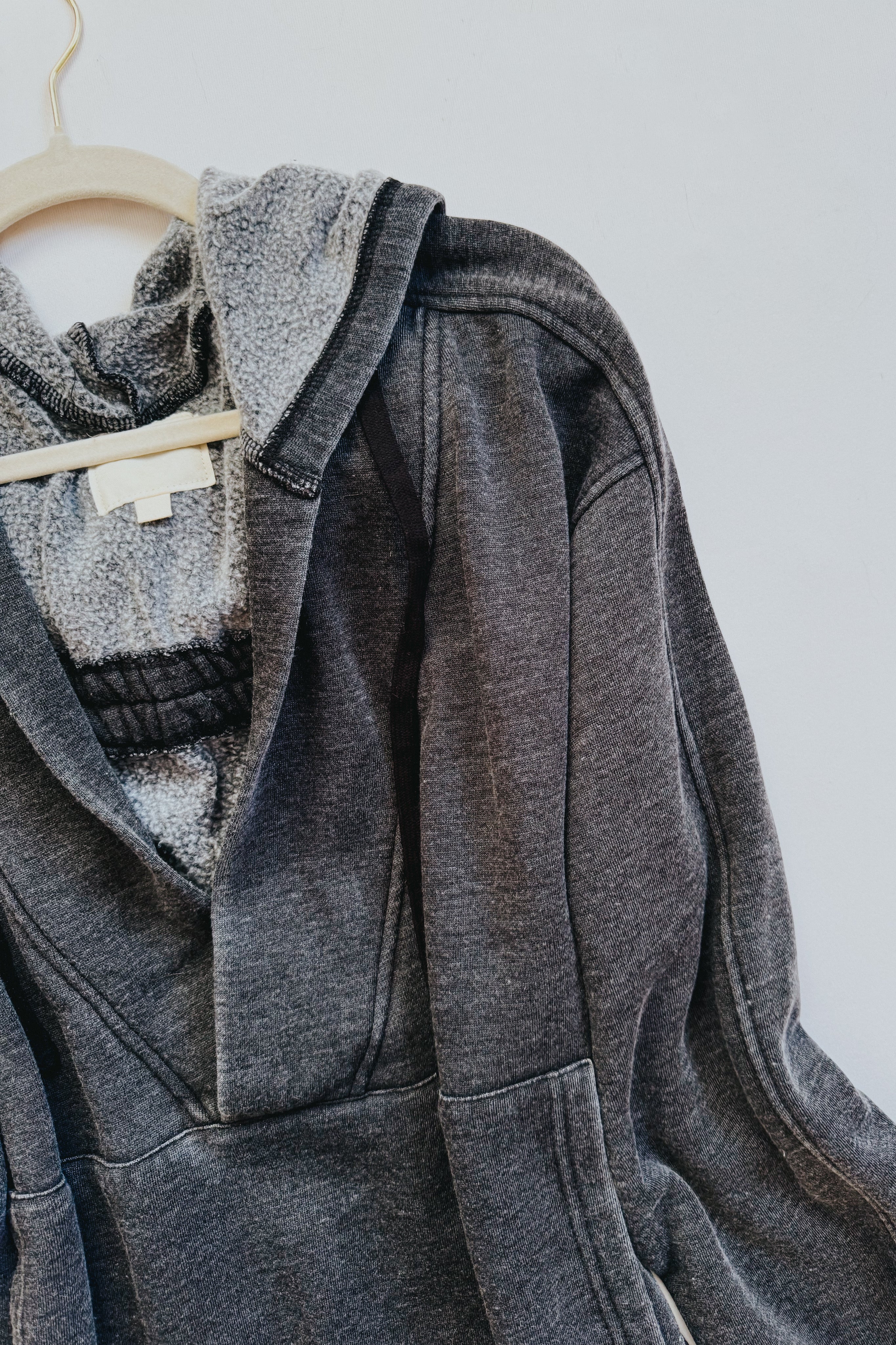 Charcoal acid wash hoodie with plush sherpa lining draped on wooden hanger against white background