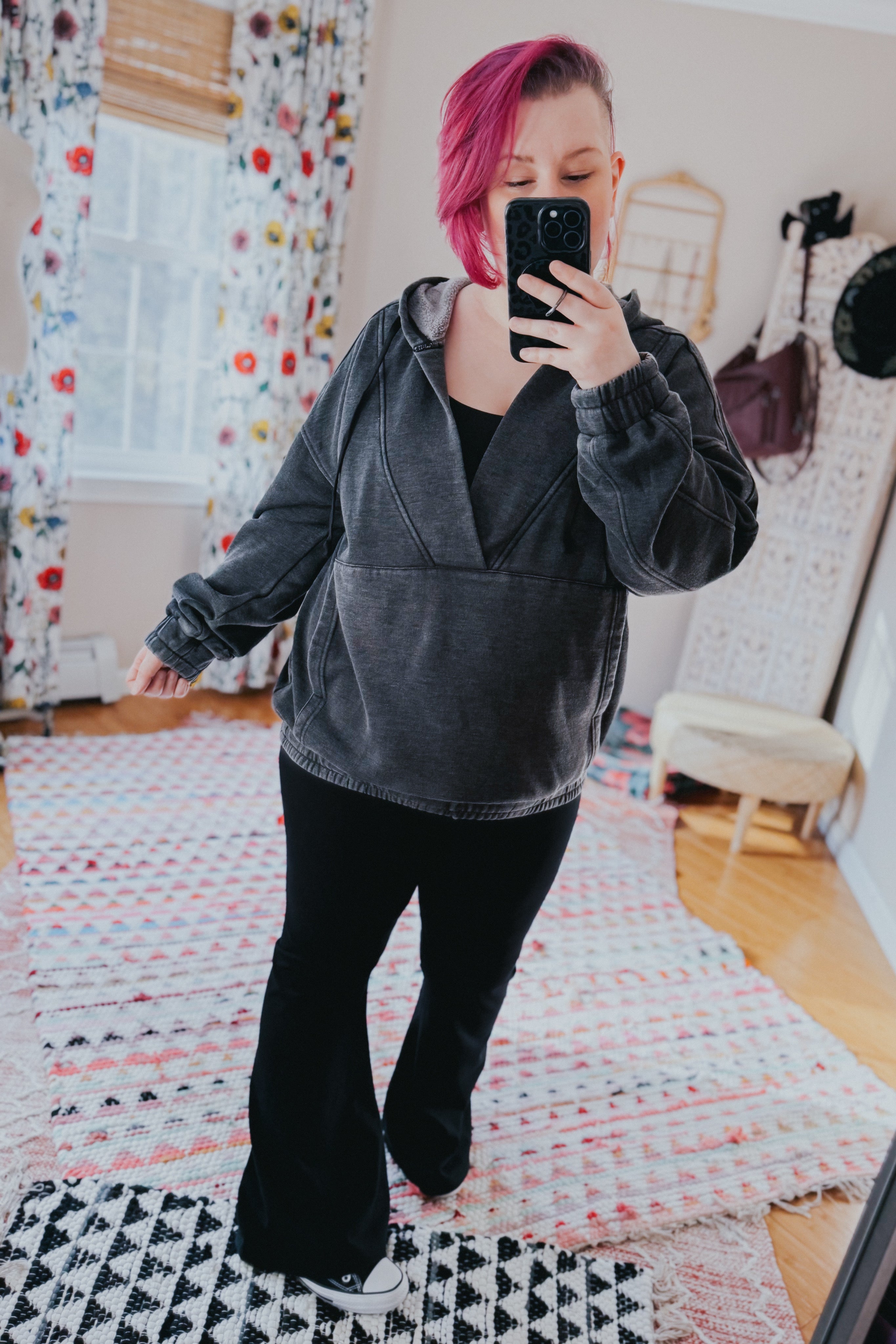 Woman with pink hair wearing charcoal acid wash hoodie paired with black flared pants taking mirror selfie indoors