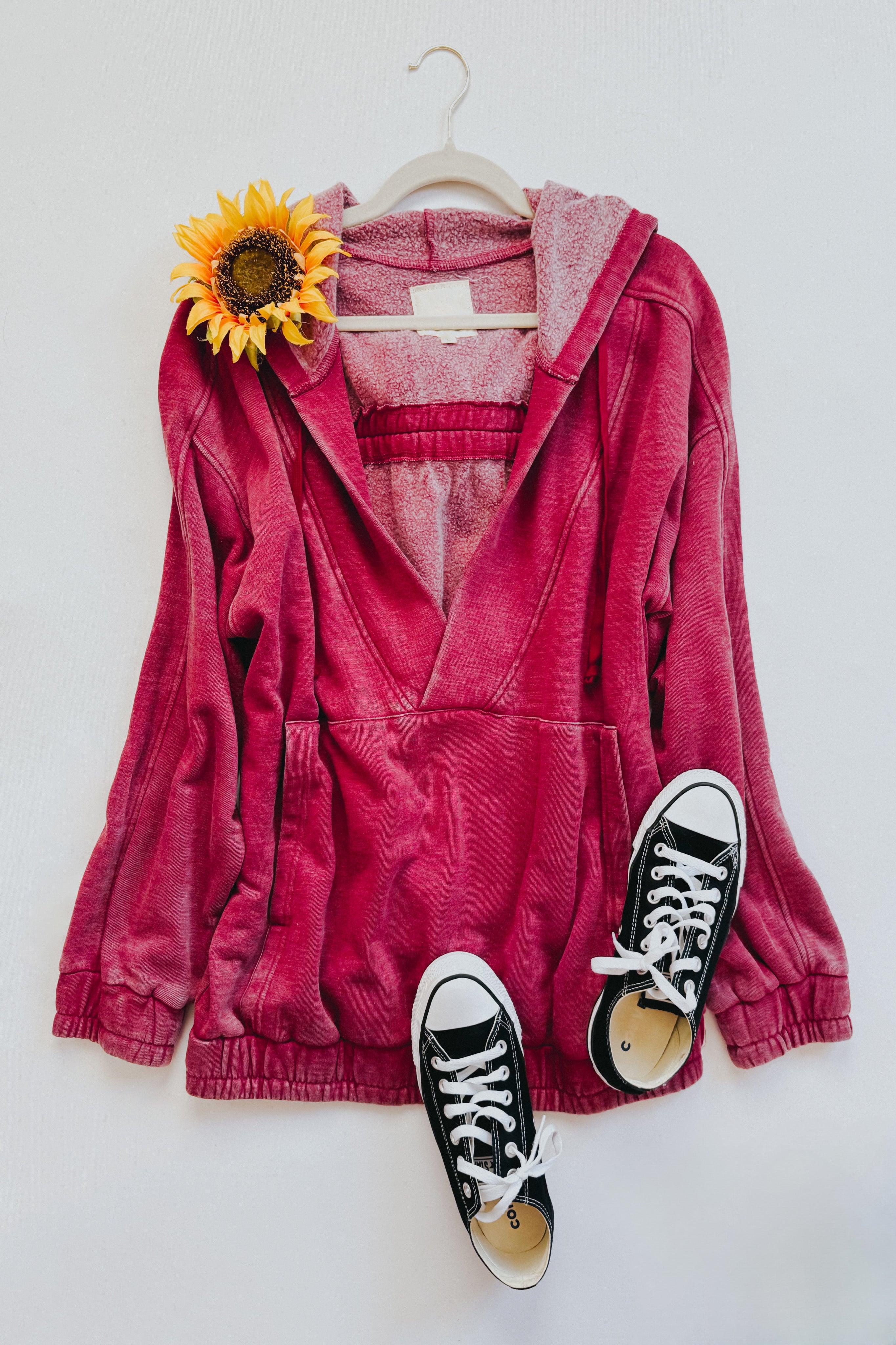 Wine-colored acid wash hoodie with hood and front pocket hanging with black sneakers and sunflower accent