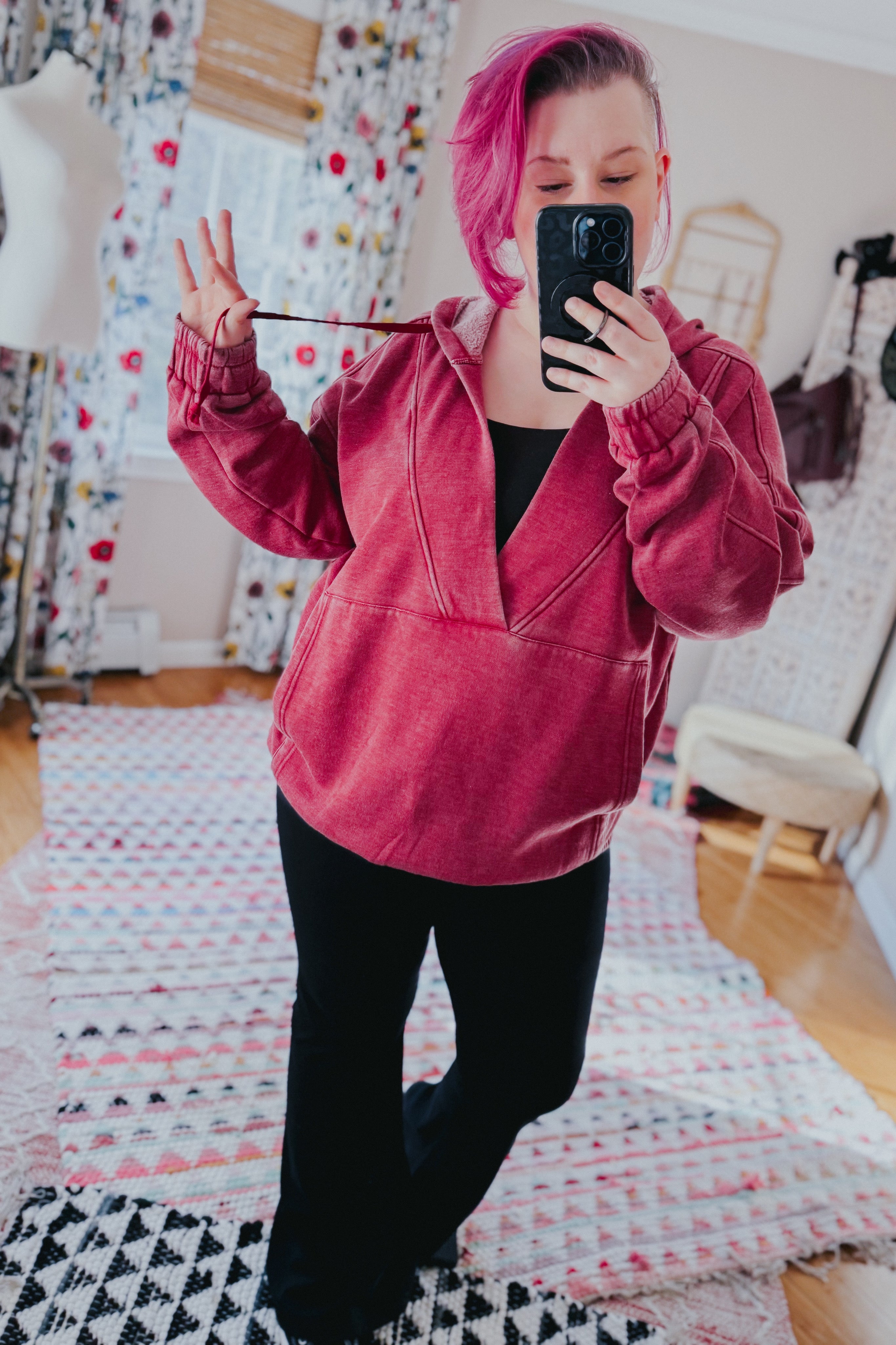 Woman with pink hair wearing wine-colored acid wash hoodie with gathered cuffs taking indoor mirror selfie