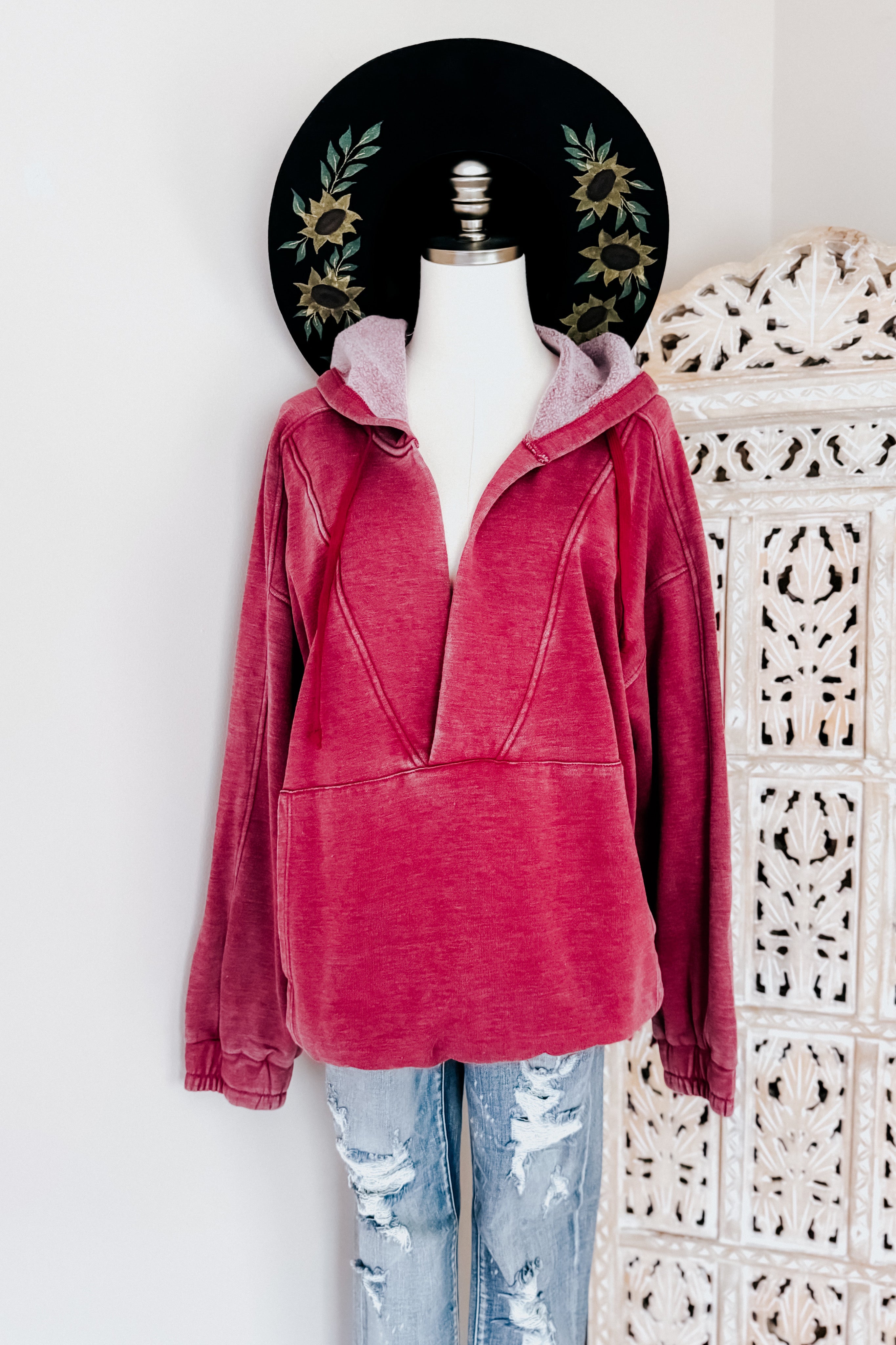 Wine-colored acid wash hoodie with deep V-neck and hood displayed with distressed jeans on mannequin