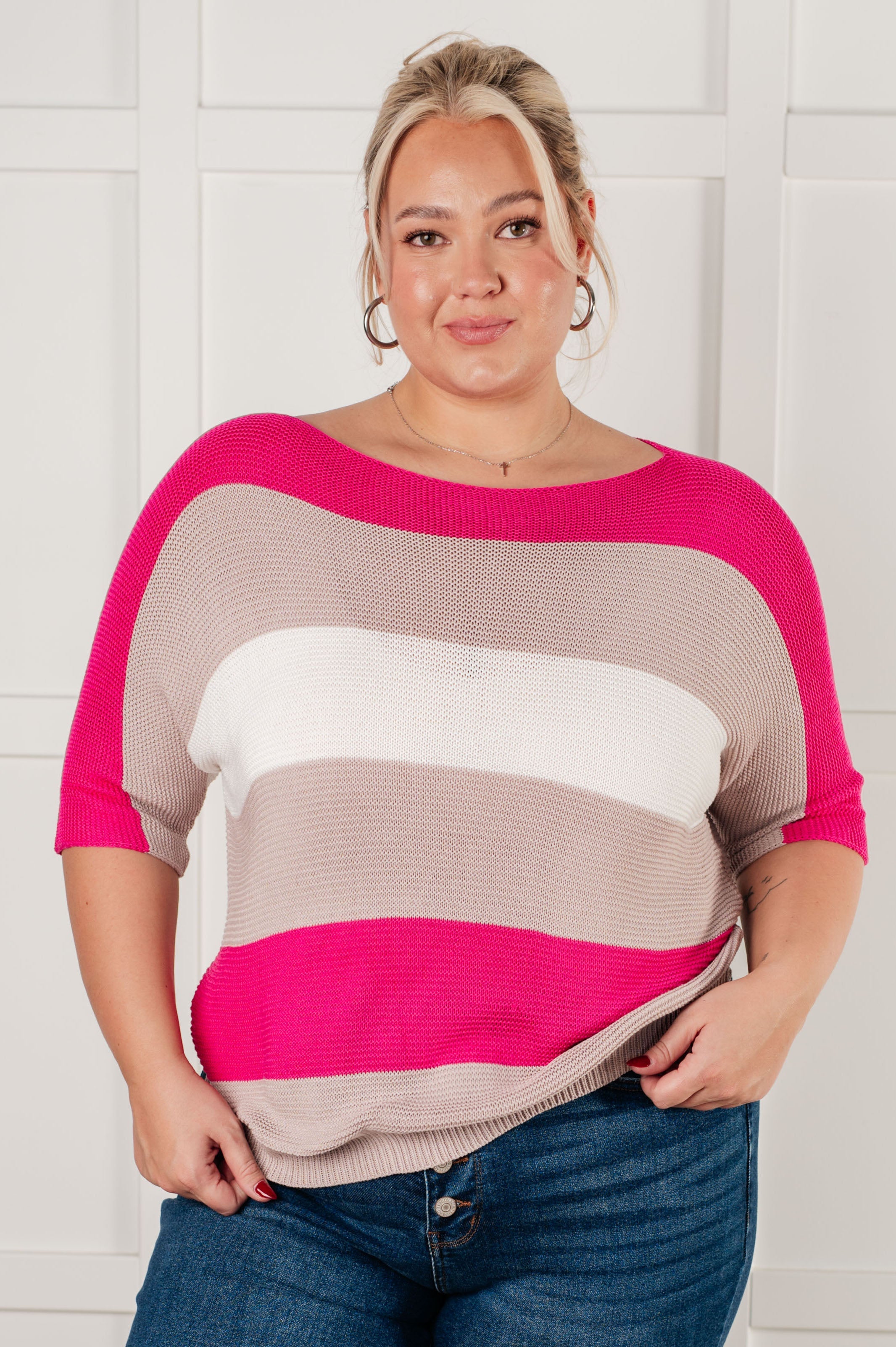 Woman wearing pink, white, and beige striped short sleeve knit top with boat neckline and hoop earrings