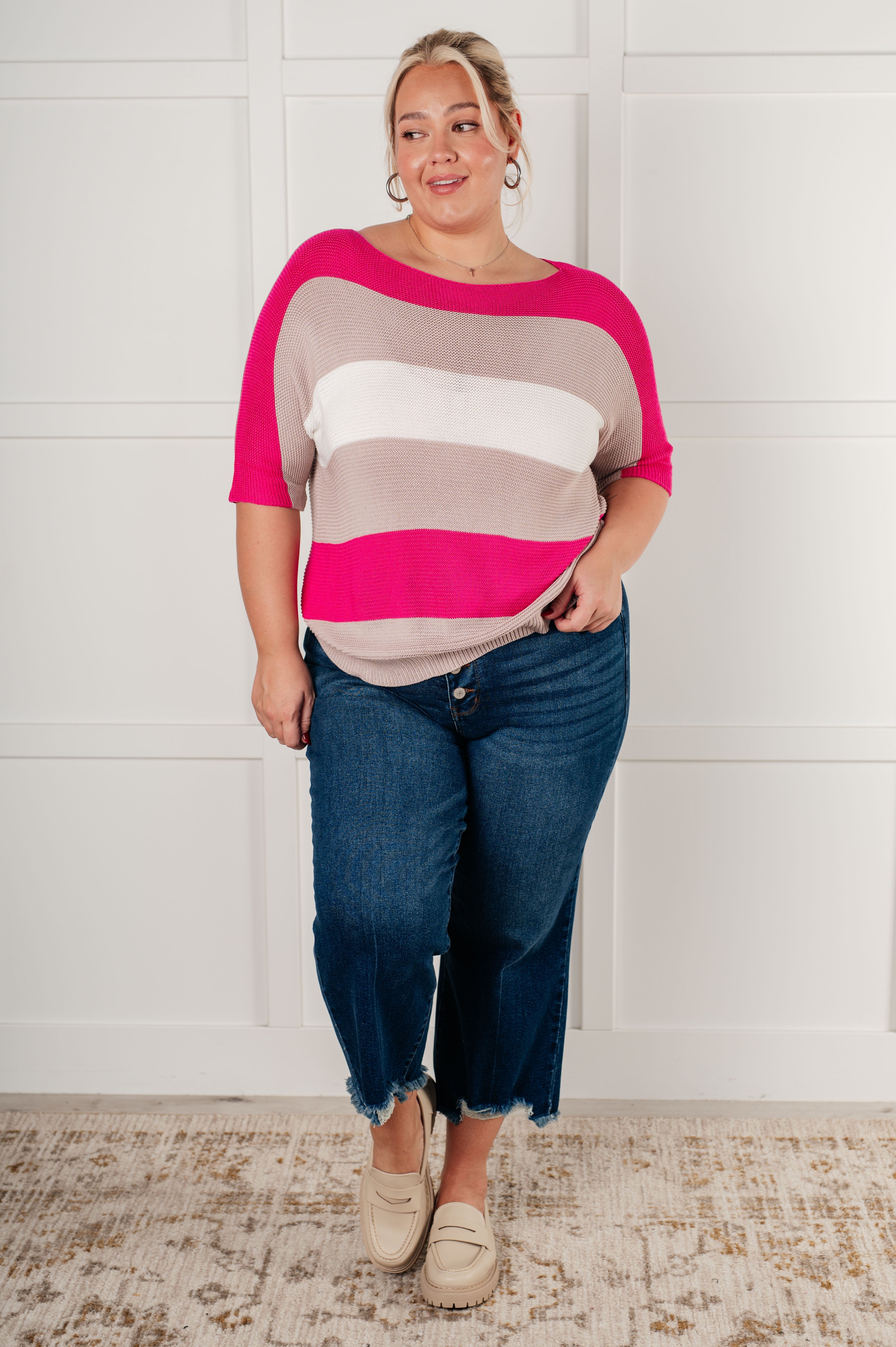 Plus size model wearing a pink and neutral striped short sleeve knit top with dark jeans and cream loafers