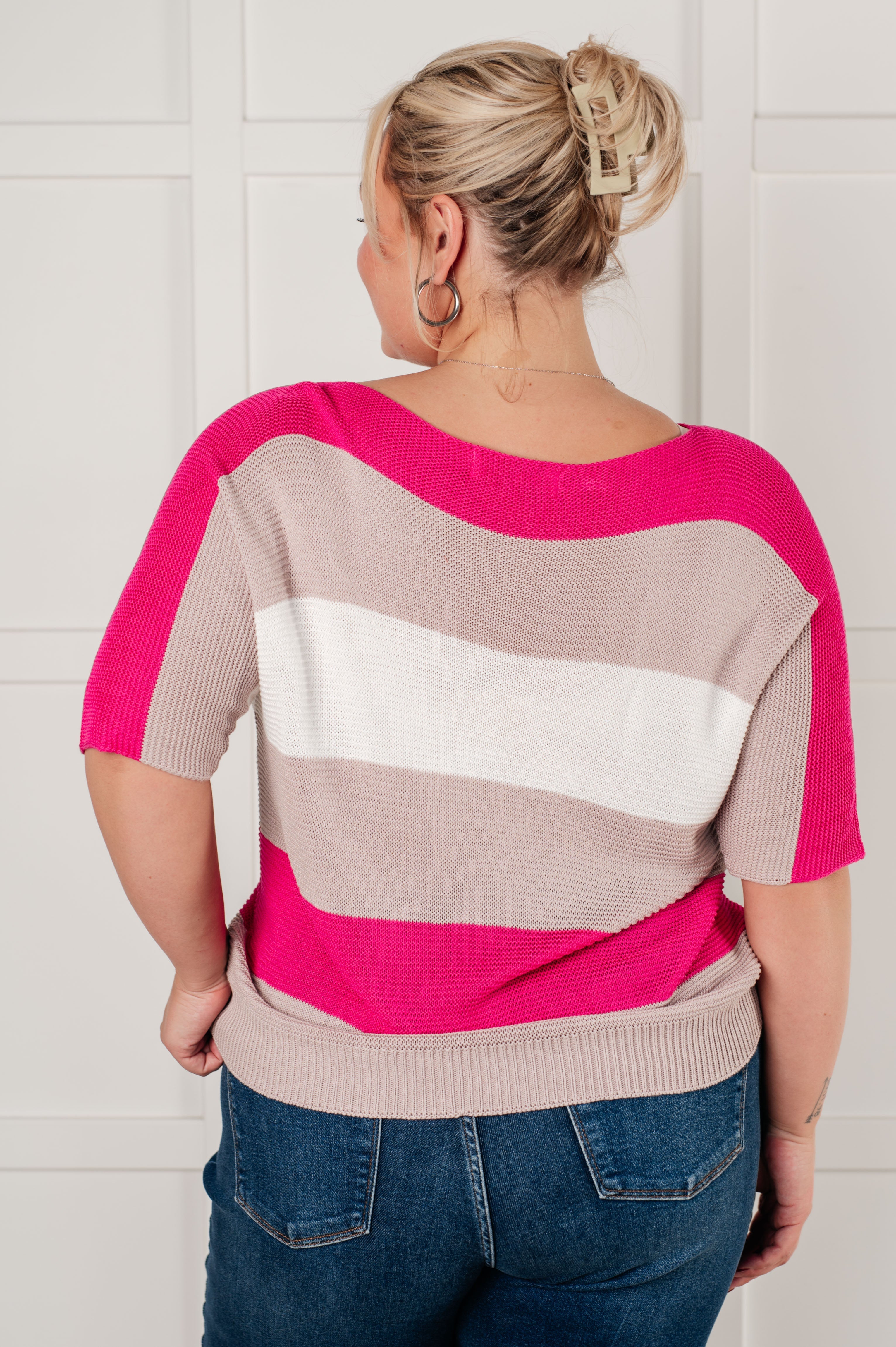 Back view of pink and beige striped knit top with short sleeves worn with blue jeans and hair clipped up