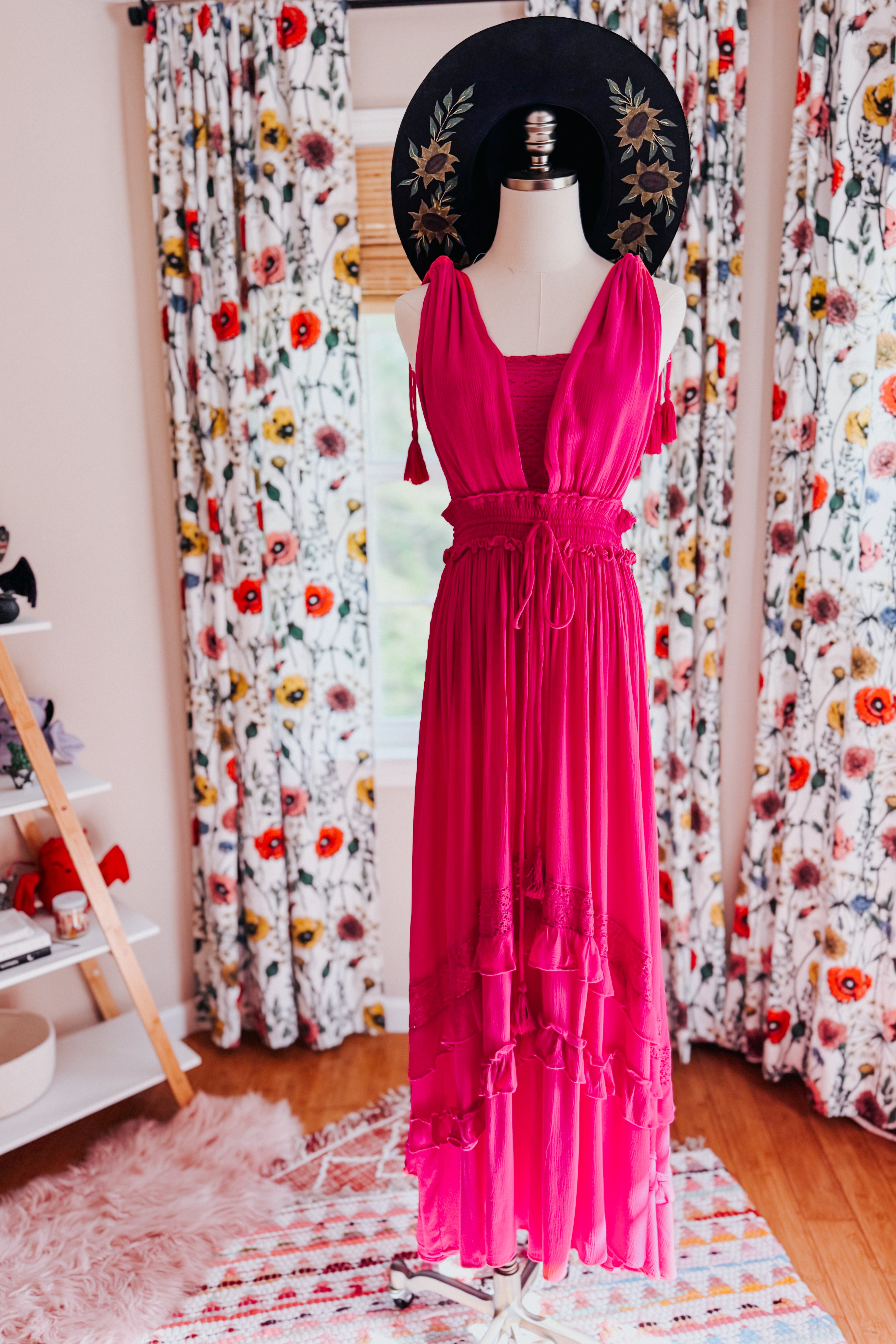 Fuchsia ruffled maxi dress with adjustable waist and deep neckline styled on mannequin with black floral hat