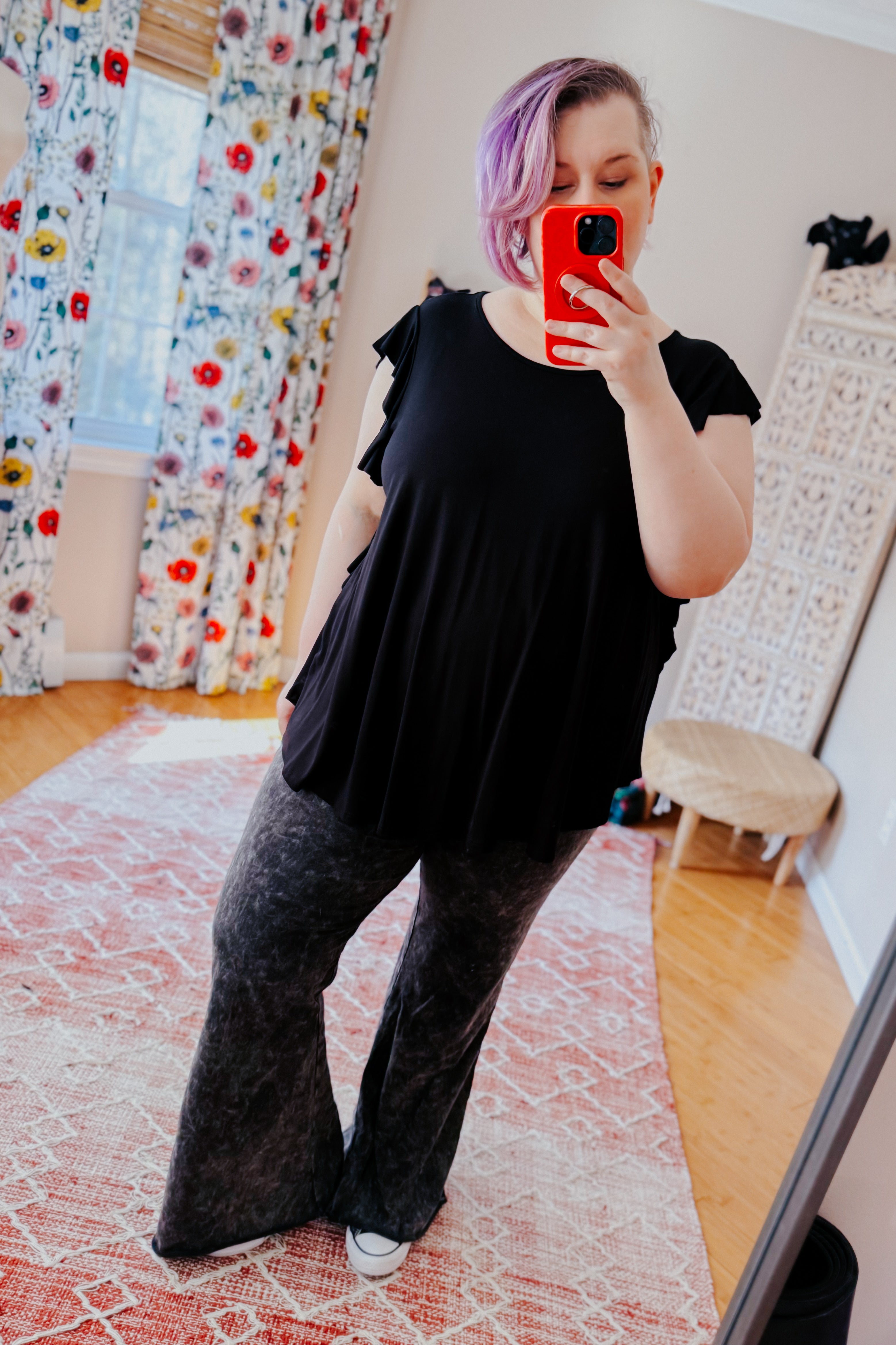 Woman wearing black ruffle sleeve top paired with charcoal flared pants taking mirror selfie indoors