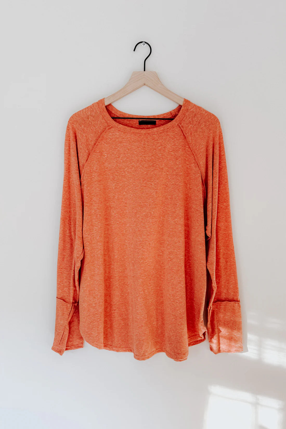 Orange long sleeve top with relaxed fit hanging on wooden hanger against light background