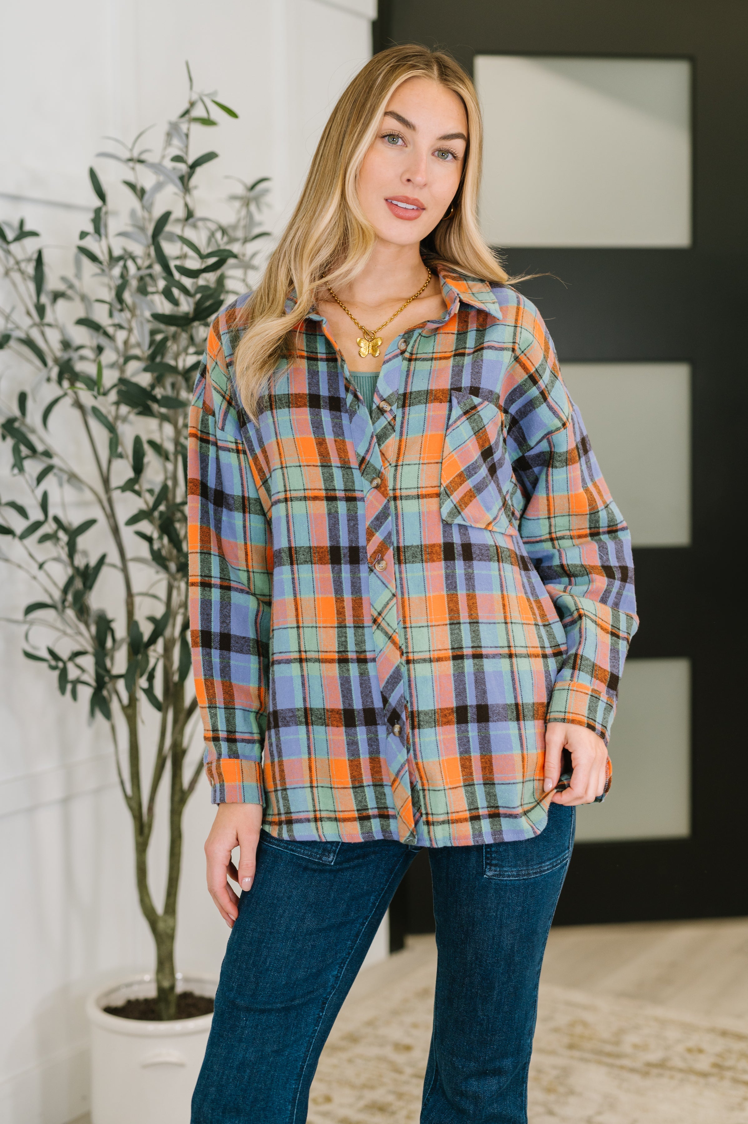 Woman wearing relaxed fit plaid button down in blue and orange tones paired with dark jeans indoors